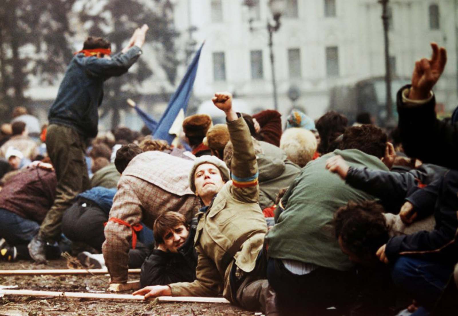 An anti-Ceaucescu revolutionary makes a V-sign as demonstrators lie on the ground to escape from the crossfire between the pro-Ceausescu troops and anti-regime supporters.