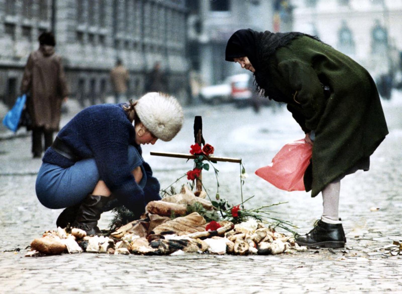 A student tends a small shrine in the middle of the main street outside Bucharest university watched by an old woman.