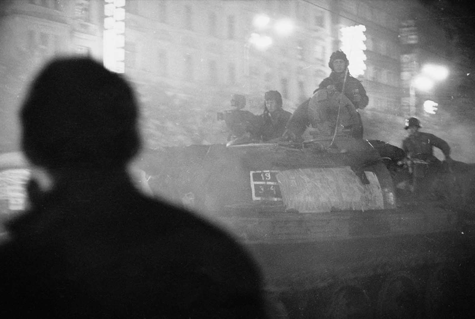 A shadowy figure watches Soviet tanks advance through the streets of Prague after nightfall in August 1968.