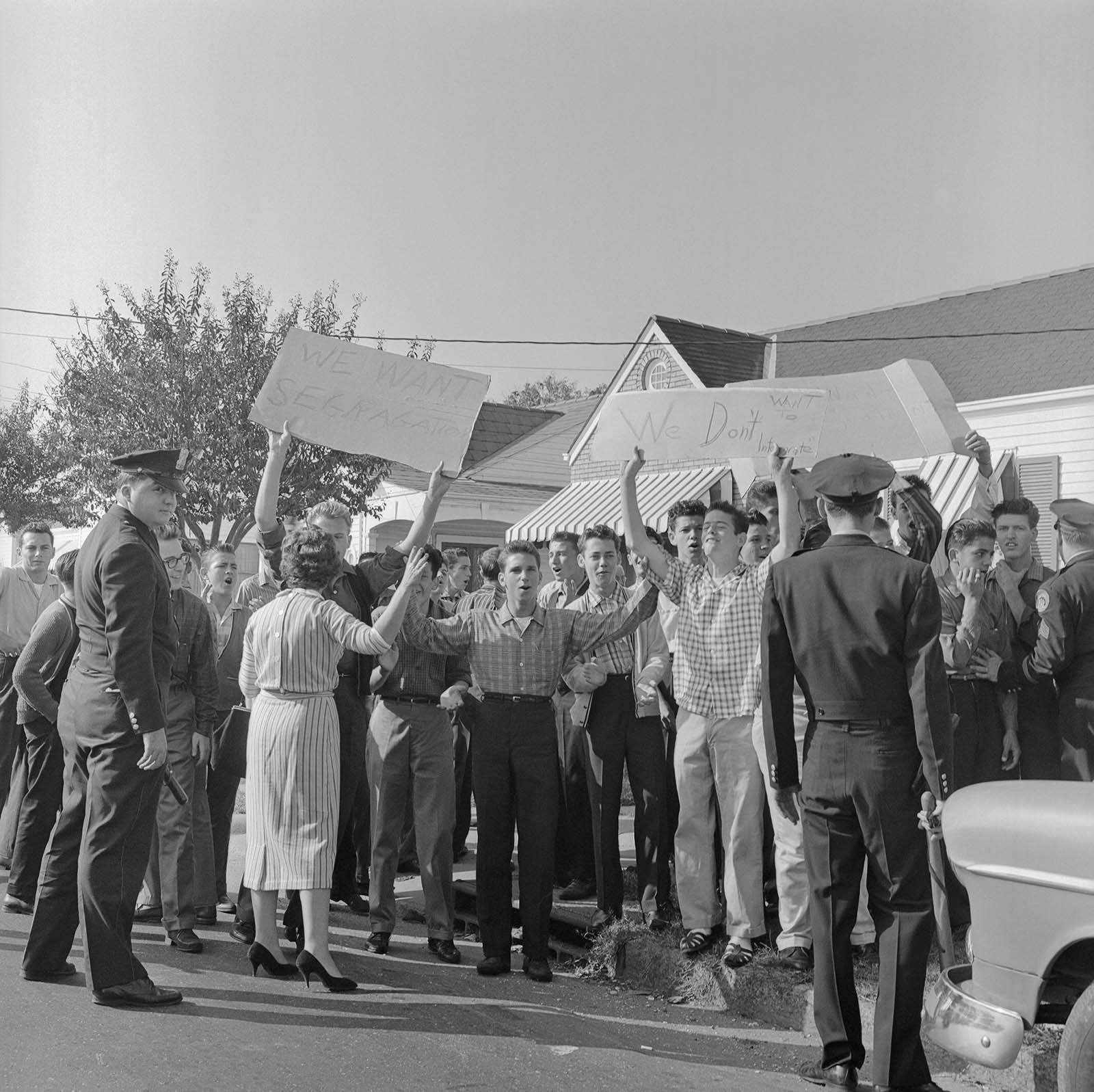 Original caption: Police keep an eye on demonstrators across the street from William Frantz Elementary School as a Negro girl entered the first grade there November 14.