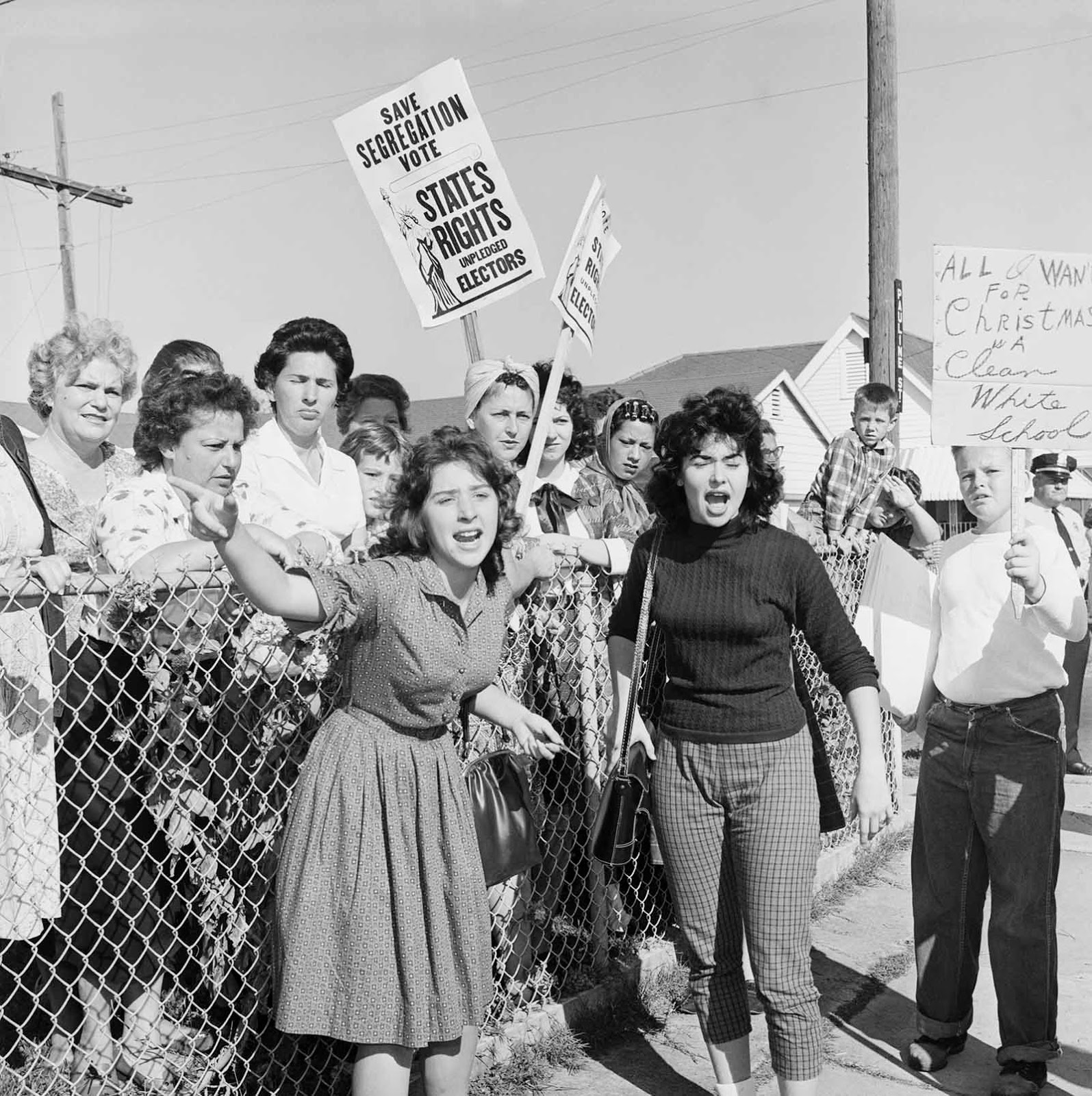 Women at William Franz Elementary School yell at police officers during a protest against desegregation of the school. Some carry signs stating