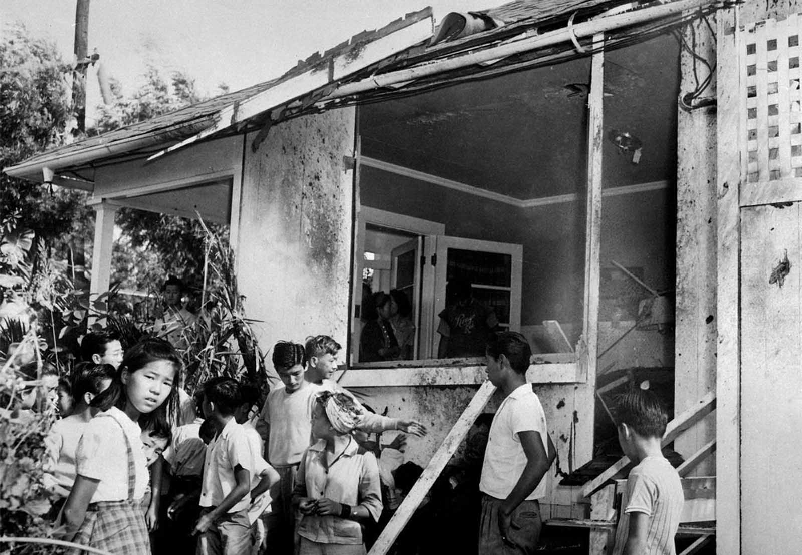 A small crowd inspects the damage, both inside and outside, after a Japanese bomb hit the residence of Paul Goo during the Japanese air raid on December 7, 1941.