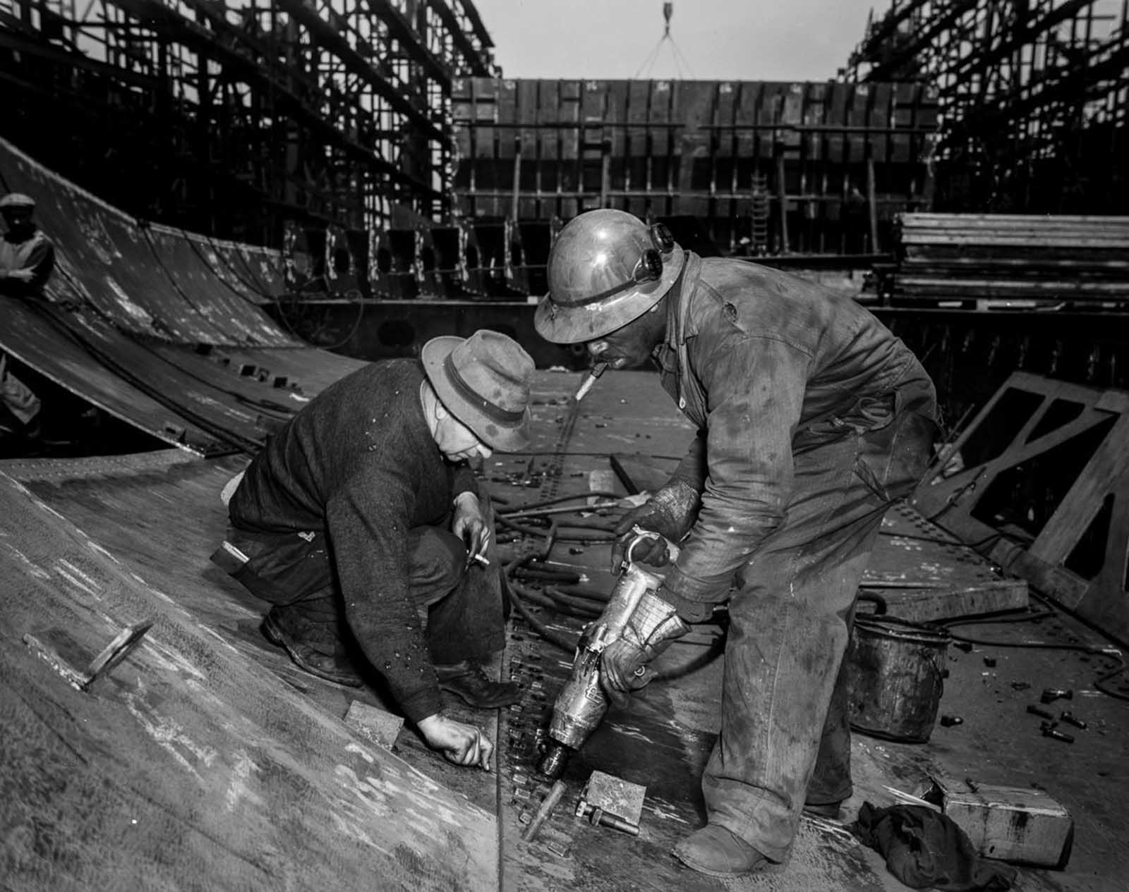 Workers tighten bolts with a pneumatic wrench in the belly of the Frederick Douglass.