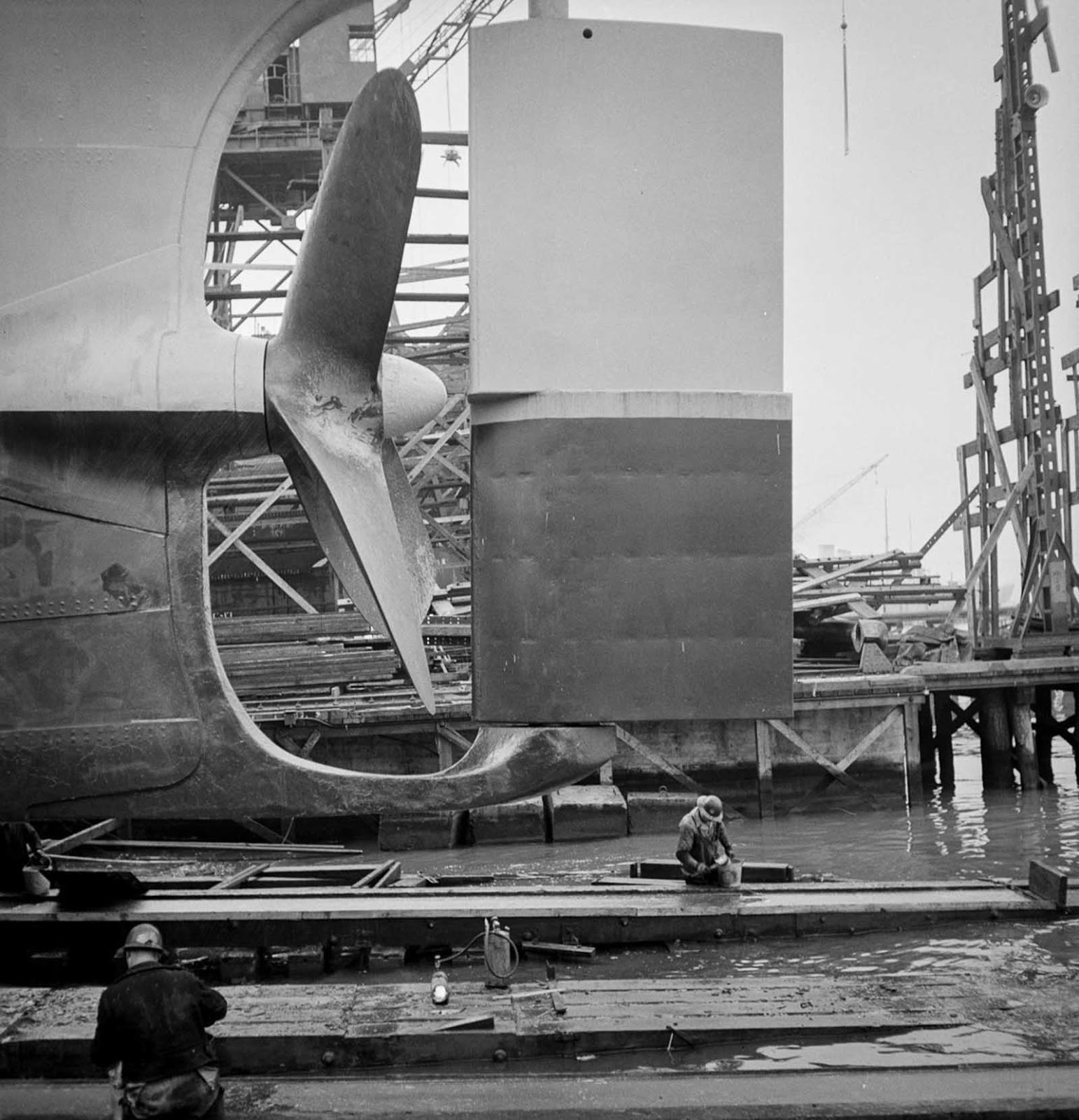 Workers grease the outboard end of a way before a launching.