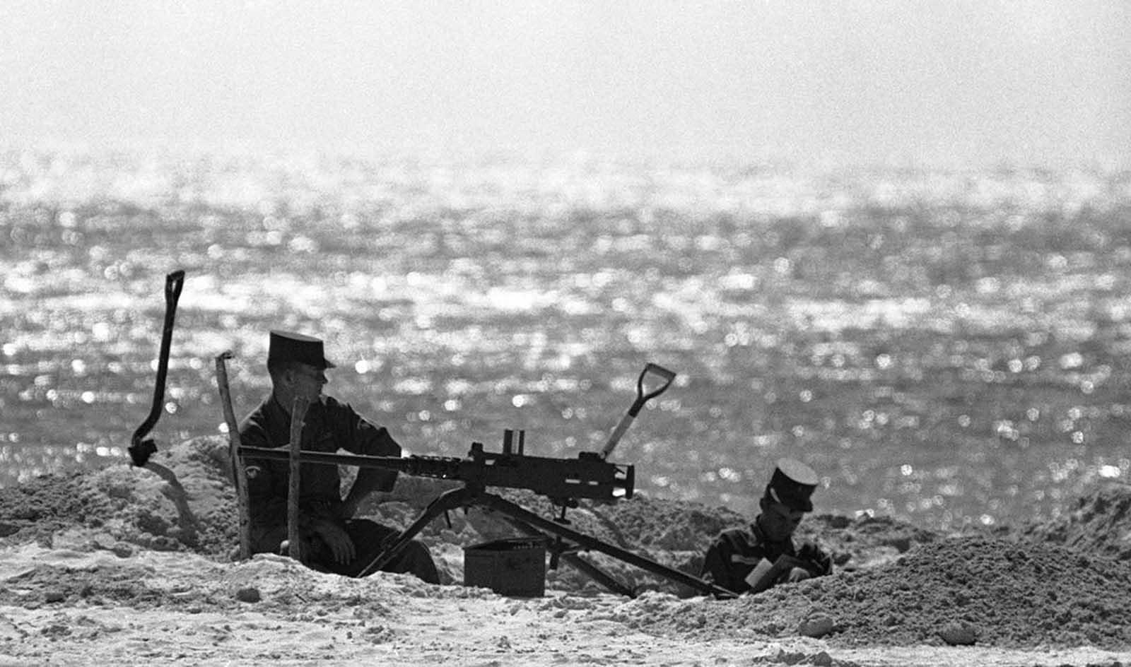 Two soldiers sit in a sandy dugout beside a machine gun hold position on a beach on Key West, Florida, on October 27, 1962.