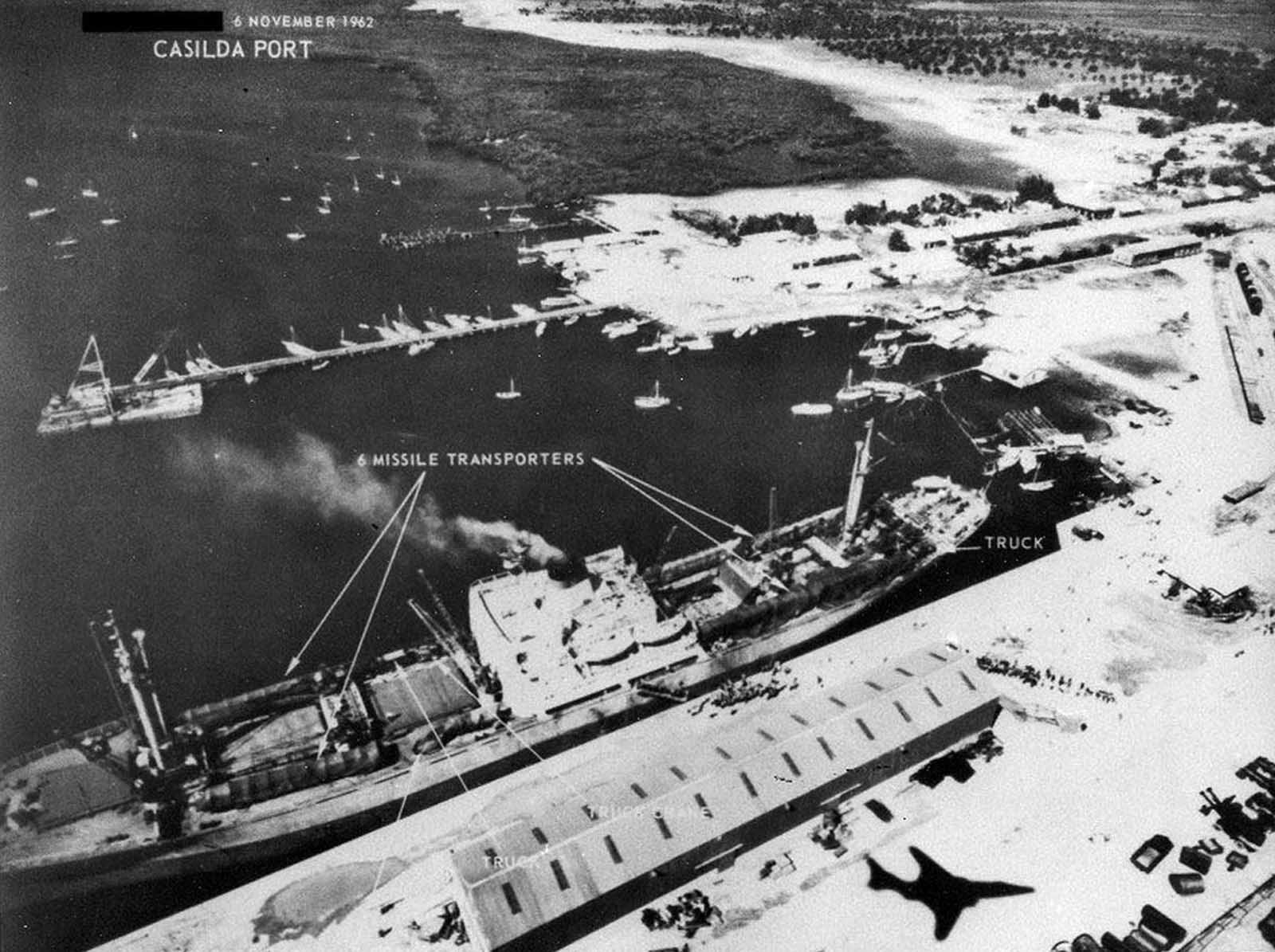 Soviet personnel and six missile transporters loaded onto a Soviet ship in Cuba's Casilda port, on November 6, 1962. Note shadow at lower right of the RF-101 reconnaissance jet taking the photograph.