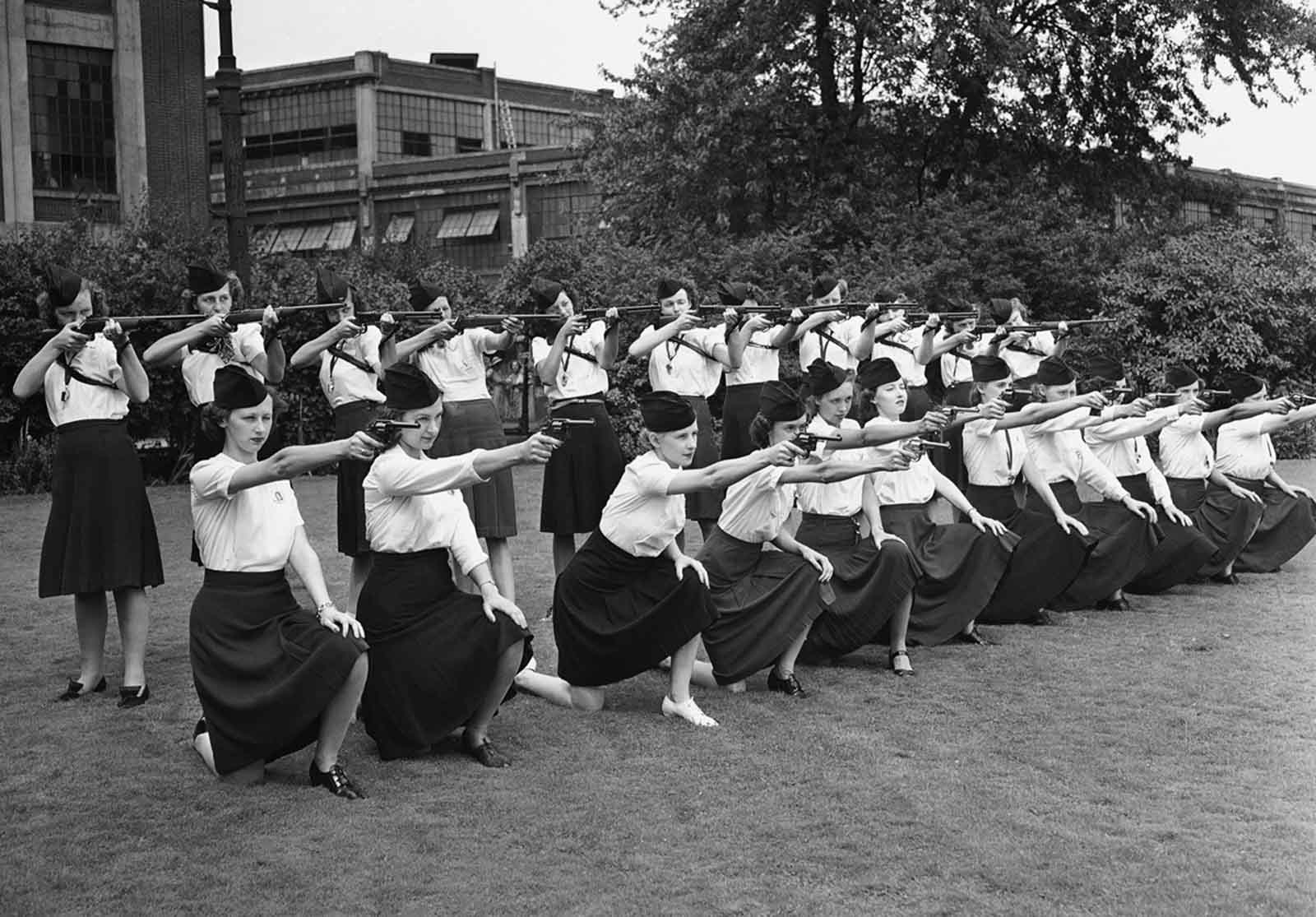Female guards, placed on duty at the Naval Ordnance Plant, operated by the Hudson Motor Car Company in Detroit, Michigan, learn how to sight guns on August 7, 1942. In the front row, the girls sight 38 caliber police pistols; those in the back row with 30-30 rifles. At present the girls are unarmed, serving only as escorts for persons entering the plant, but are using weapons on the target range in preparation.