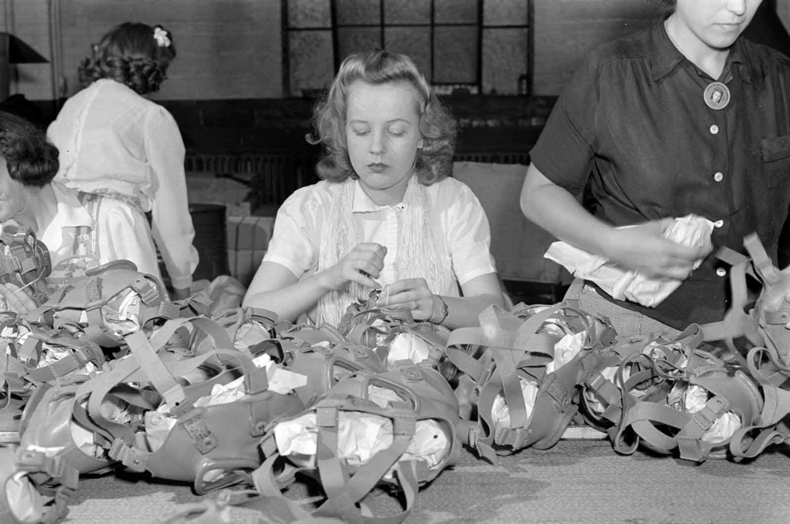 Gas mask production. Lacing head harnesses of gas masks after they have passed through all the stages of assembly and made ready for packaging, is the job of this young woman who works in the Eureka Vacuum factory which has been converted to war production.