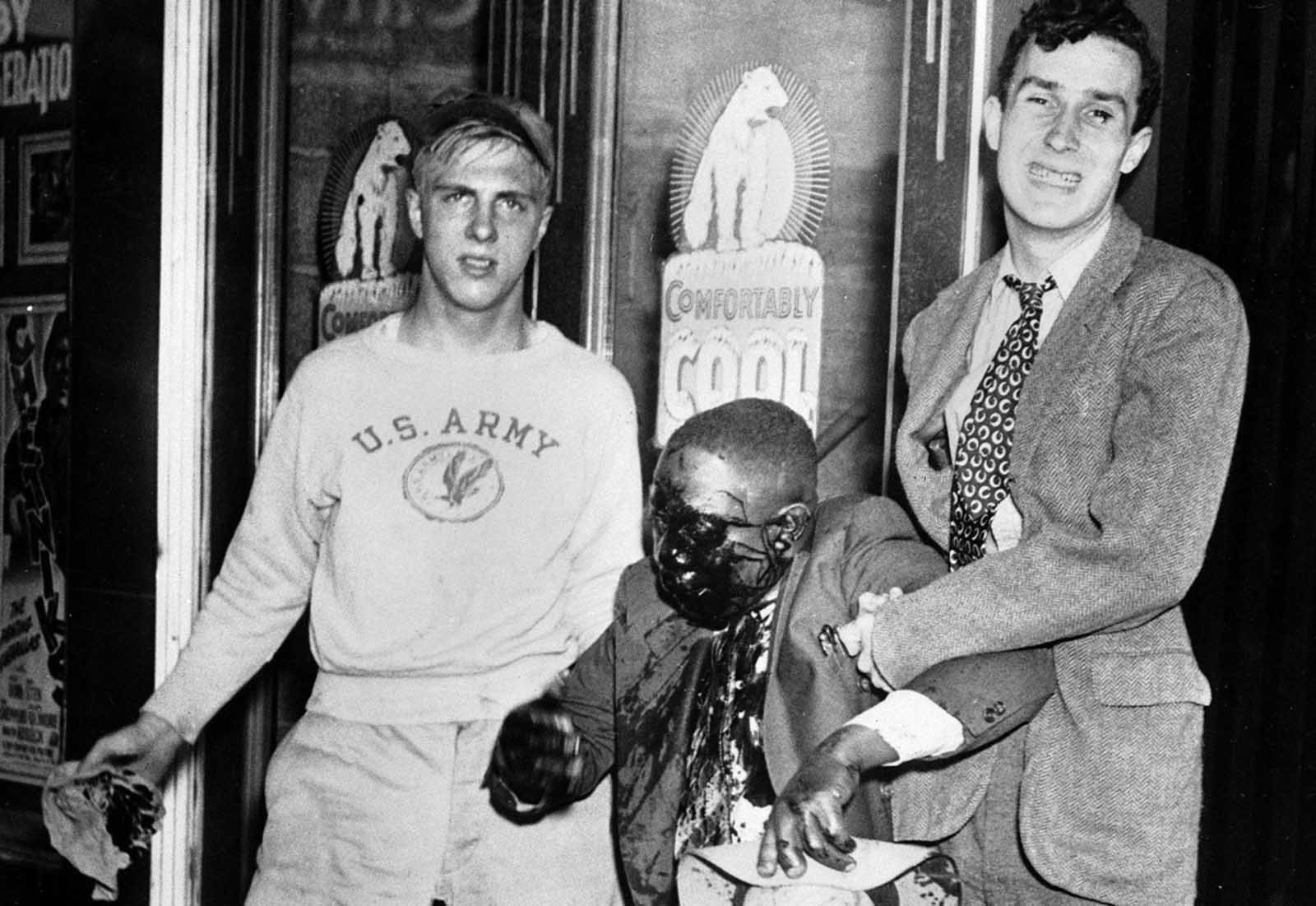 Two youths help a man to his feet after he was badly beaten in street fighting which marked race riots in Detroit, Michigan, on June 21, 1943.