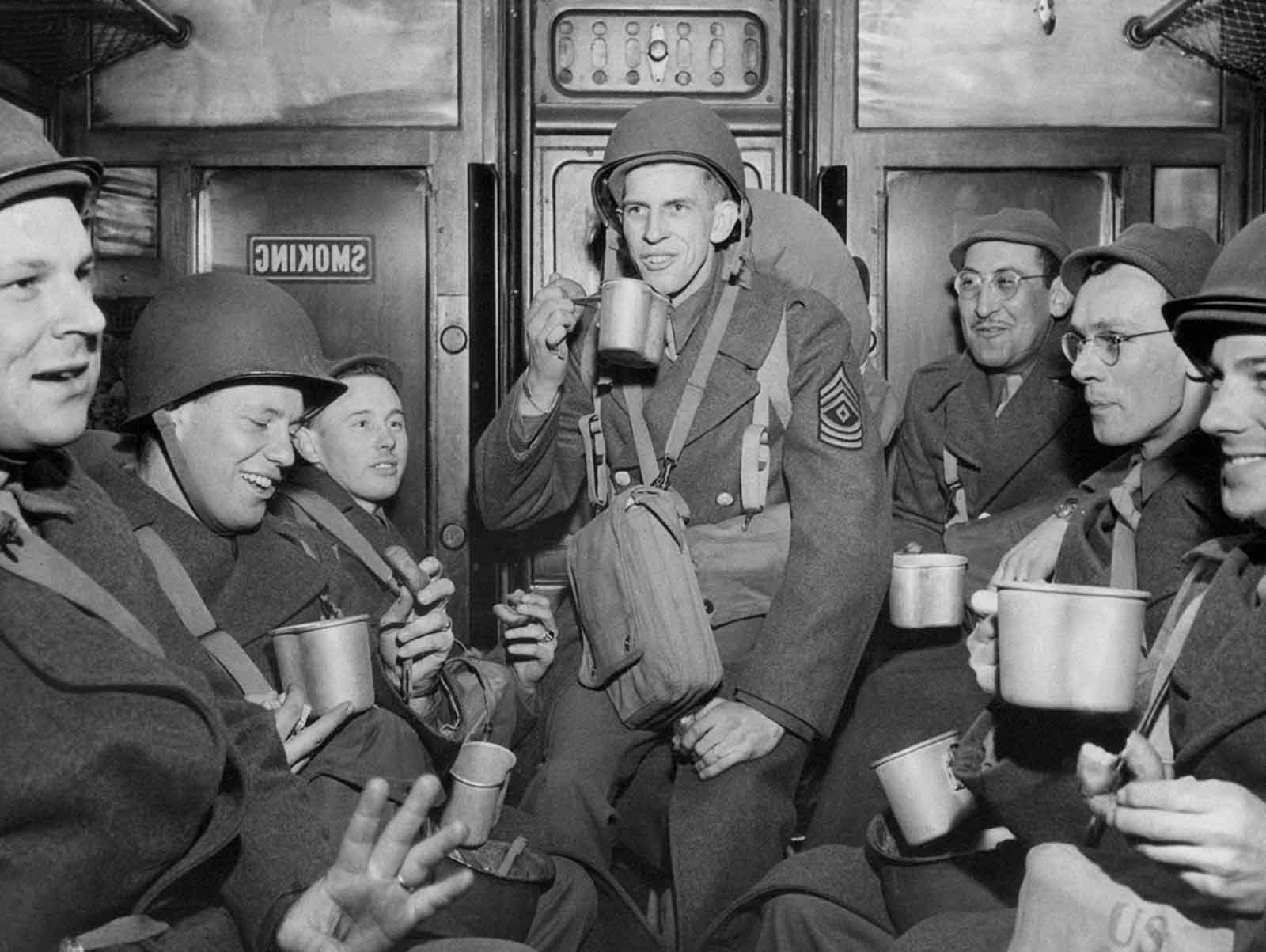 This group of soldiers who debarked from a transport drink from mugs of coffee and munch doughnuts on a troop train en route to their station in England, March 15, 1944.