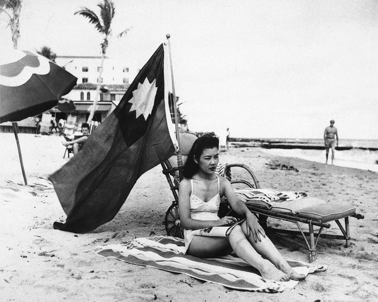 Ruth Lee, a hostess at a Chinese restaurant, flies a Chinese flag so she isn’t mistaken for Japanese when she sunbathes on her days off in Miami, in the wake of the attack on Pearl Harbor, Dec. 15, 1941. The flag shown here is the flag of Nationalist China which went into self imposed exile to the island of Taiwan after the Communist revolution. This flag is now the flag of Taiwan.