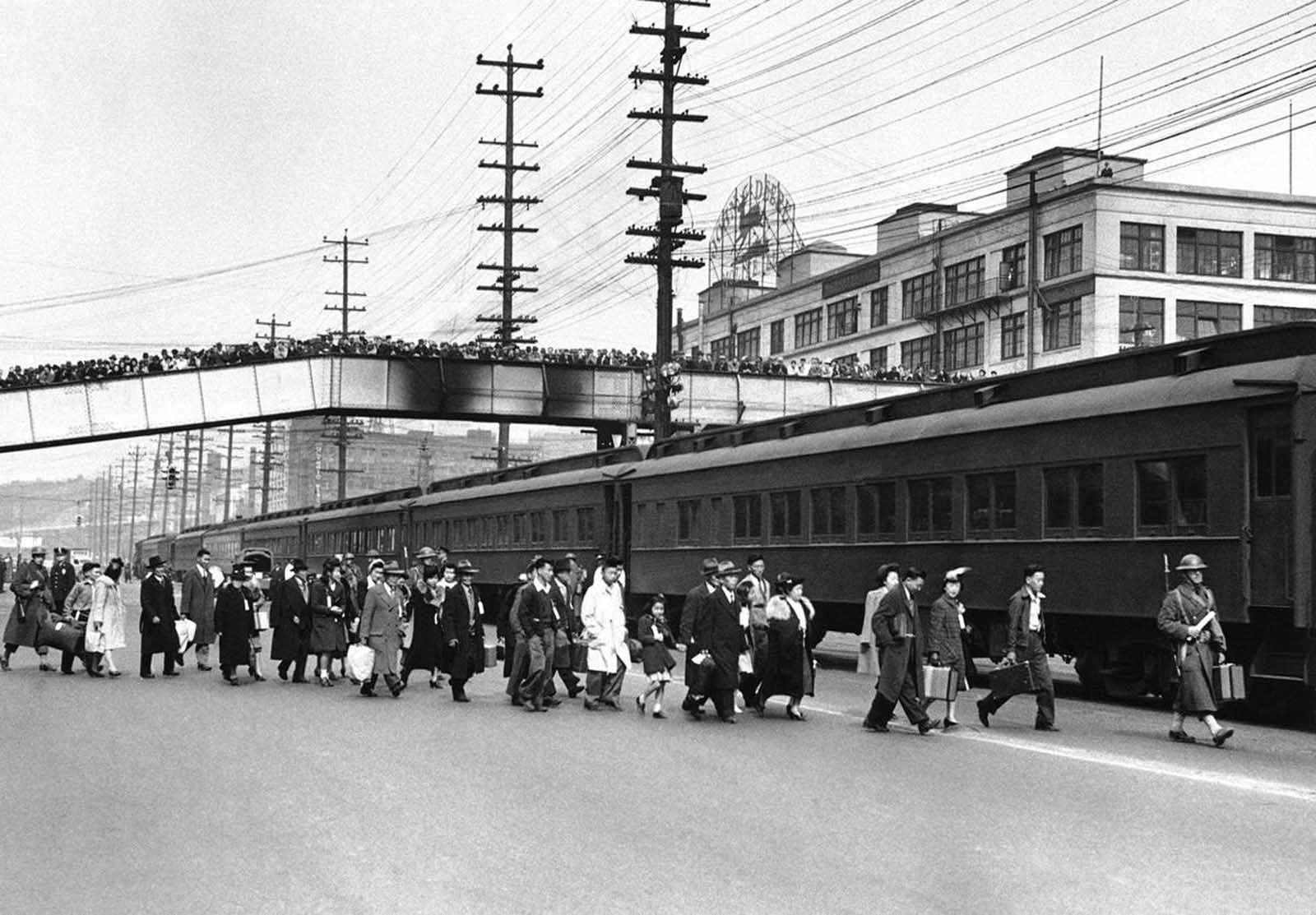 A crowd of onlookers in Seattle jam an overhead walk to witness the mass evacuation of Japanese from Bainbridge Island, Washington, on March 30, 1942. Somewhat bewildered, but not protesting, some 225 Japanese men, women and children were taken by ferry, bus and train to California internment camps. The evacuation was carried out by the U.S. Army.