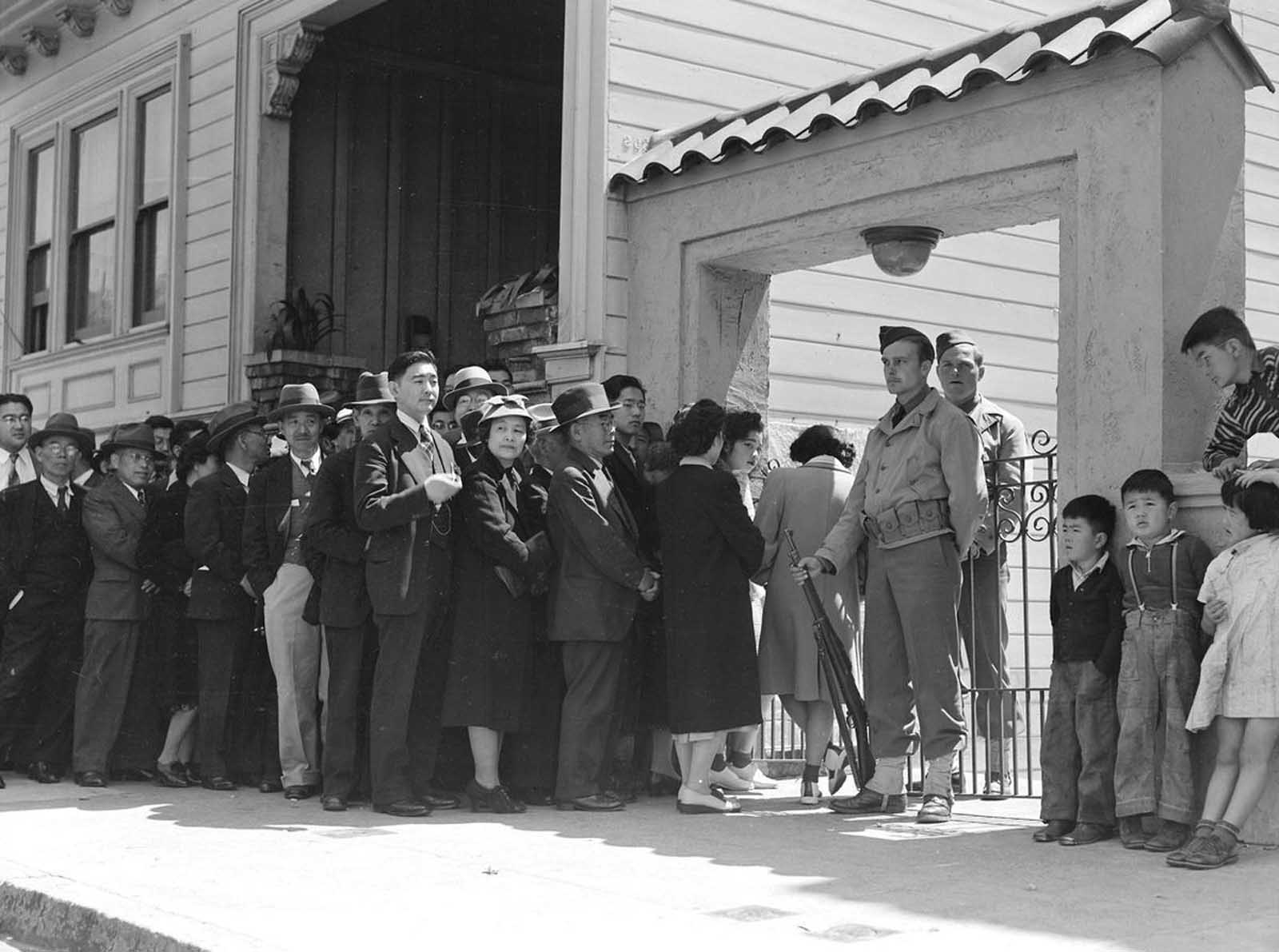 Japanese heads of family and persons living alone form a line outside Civil Control Station located in the Japanese American Citizens League Auditorium in San Francisco, California, to appear for