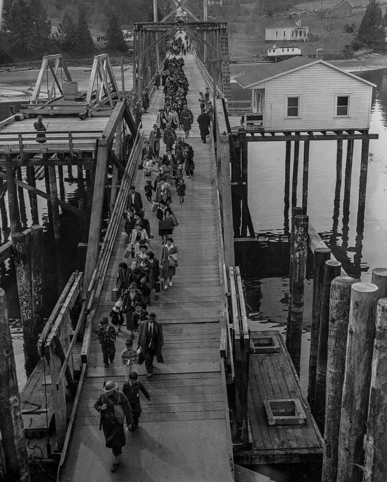 Japanese-Americans escorted by soldiers cross a bridge as they are evacuated from Bainbridge Island to be taken to a relocation camp.