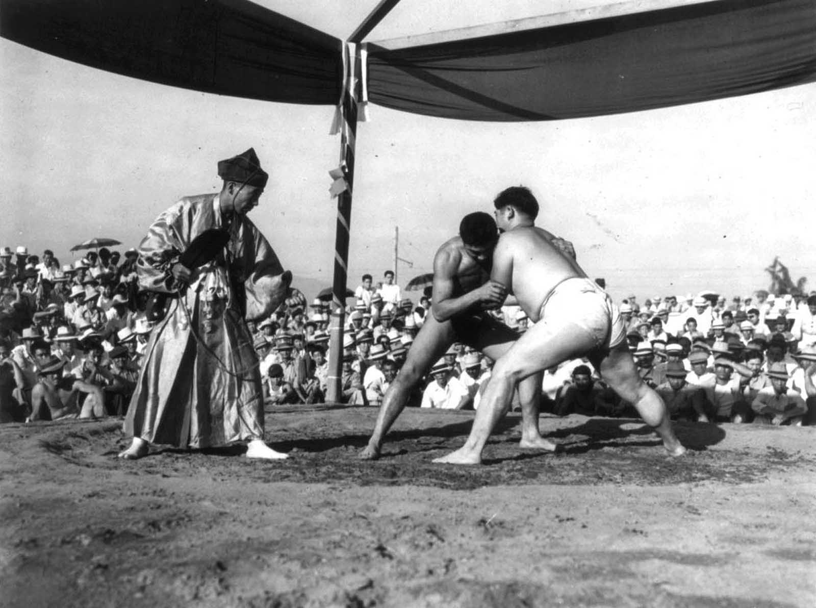 A referee in traditional dress watches over a Sumo wrestling match in front of Japanese-Americans interned at Santa Anita, California.