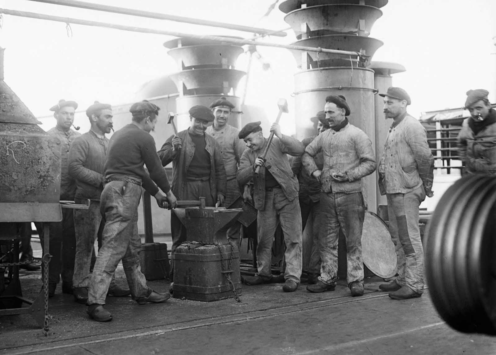 Sailors aboard the French cruiser Amiral Aube pose for a photograph at an anvil attached to the deck.