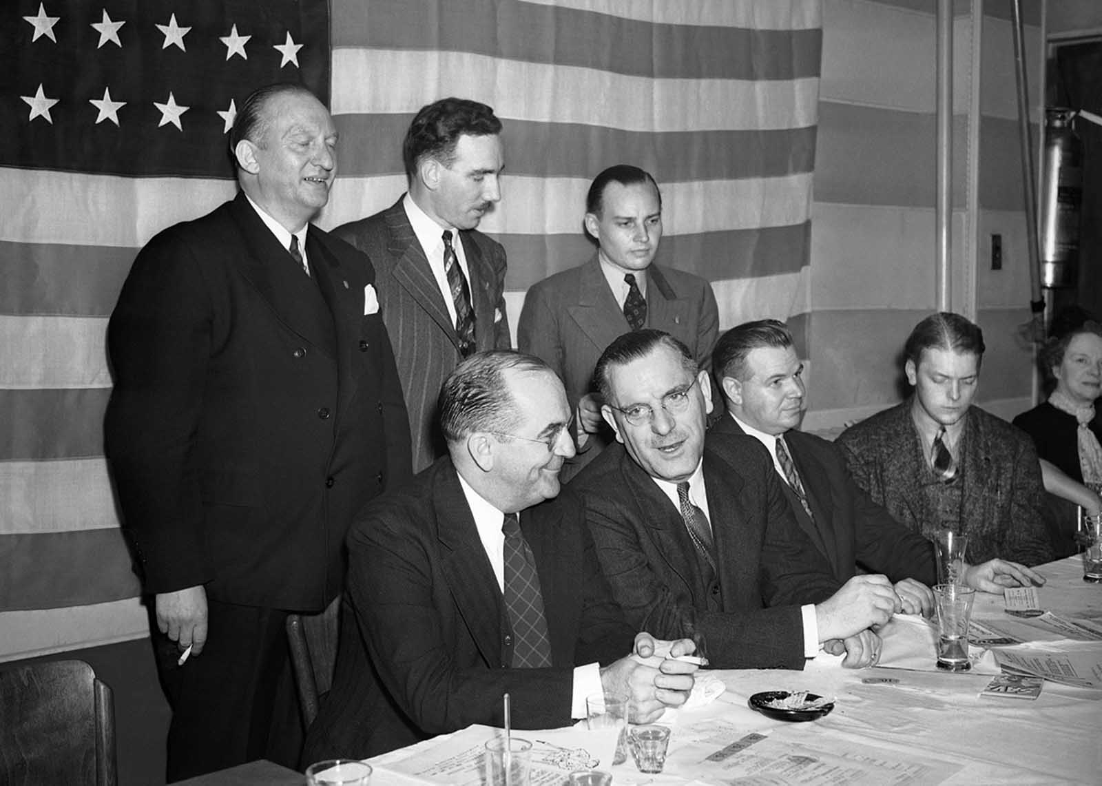 German American Bund speakers and officers in front of an American flag at a “patriotic dinner” in New York, on September 25, 1939 at which President Roosevelt’s neutrality recommendations were denounced. From left, seated Wilbur Keegan, New Jersey attorney who urged members to profess their loyalty to the United States; Fritz Kuhn, Bund fuehrer; and William Meyer, who said the Bund would continue to fight for a “real nationalistic America”. Standing: Gustave Elmer, William Kunze and James Wheeler-Hill, Bund officials.
