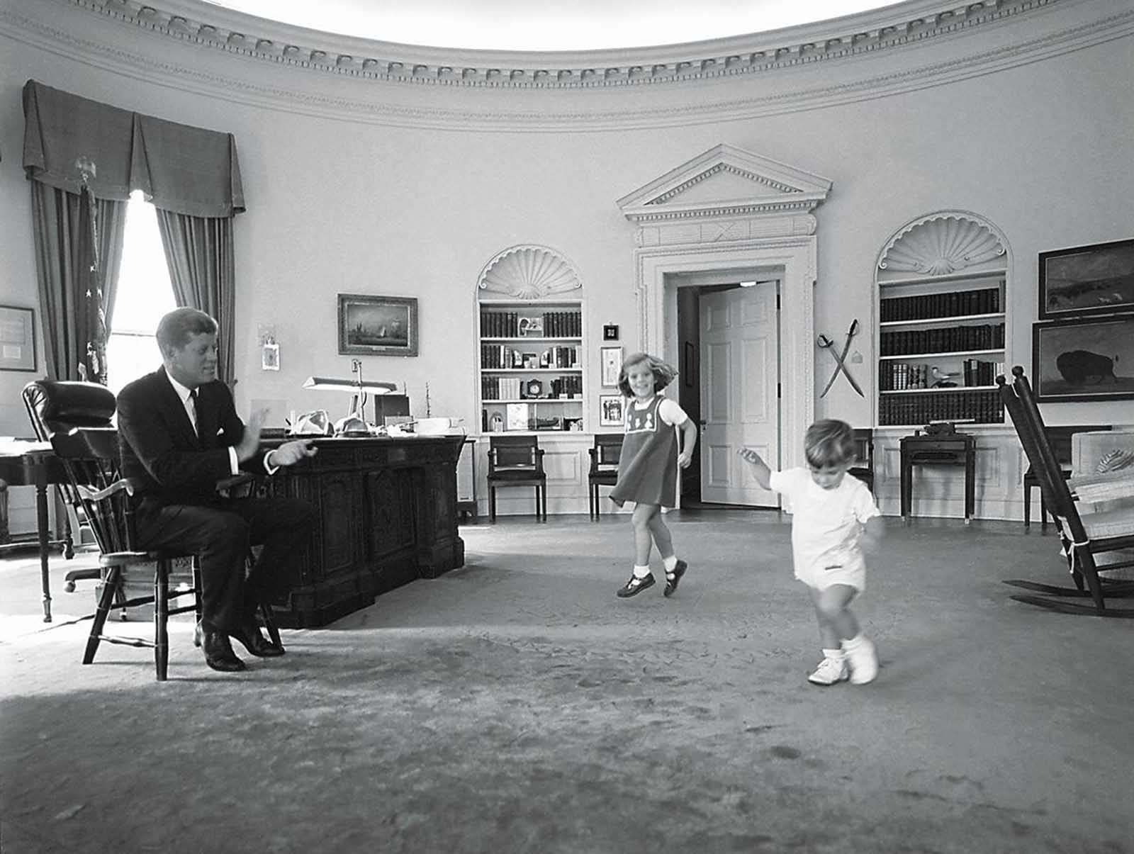 President Kennedy claps to keep time as his children Caroline and John, Jr. dance in the Oval Office, in October of 1962.