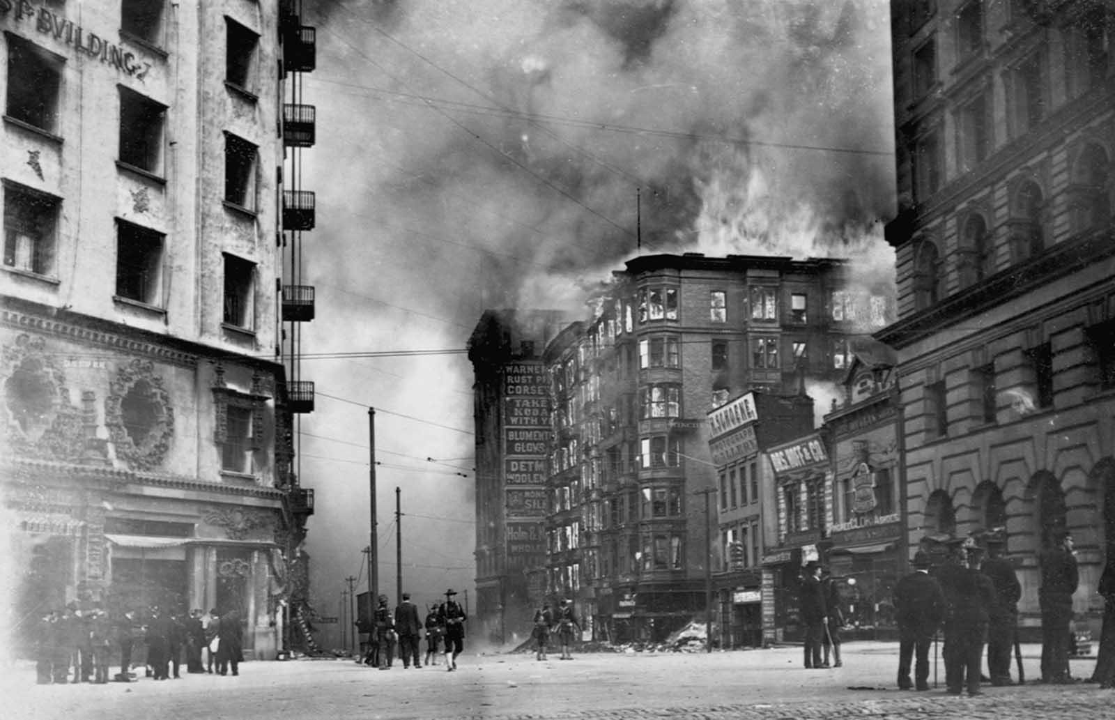 People watch as the Winchester Hotel burns in the aftermath of the 1906 San Francisco earthquake. The Hearst Building (left) was dynamited to use as a fire break between the fire and the rest of the city.