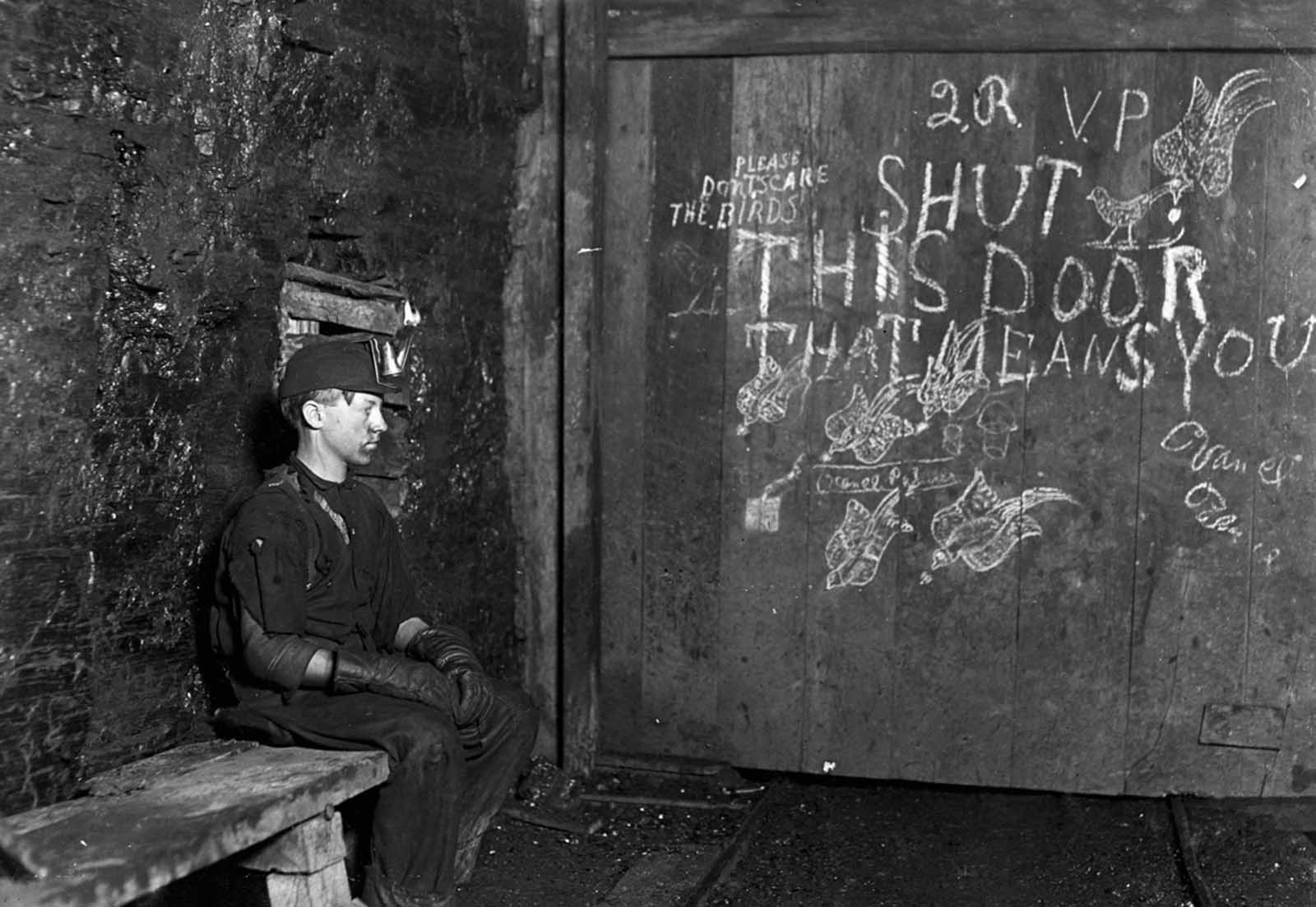 15-year-old Vance, a trapper boy, sits by a large door in West Virginia coal mine in September of 1908. Vance has trapped for several years, receiving 75 cents a day for 10 hours work. All he does is to open and shut this door. Most of the time he sits here idle, waiting for the cars to come. Due to the intense darkness in the mine, the hieroglyphics on the door were not visible until his photo plate was developed.