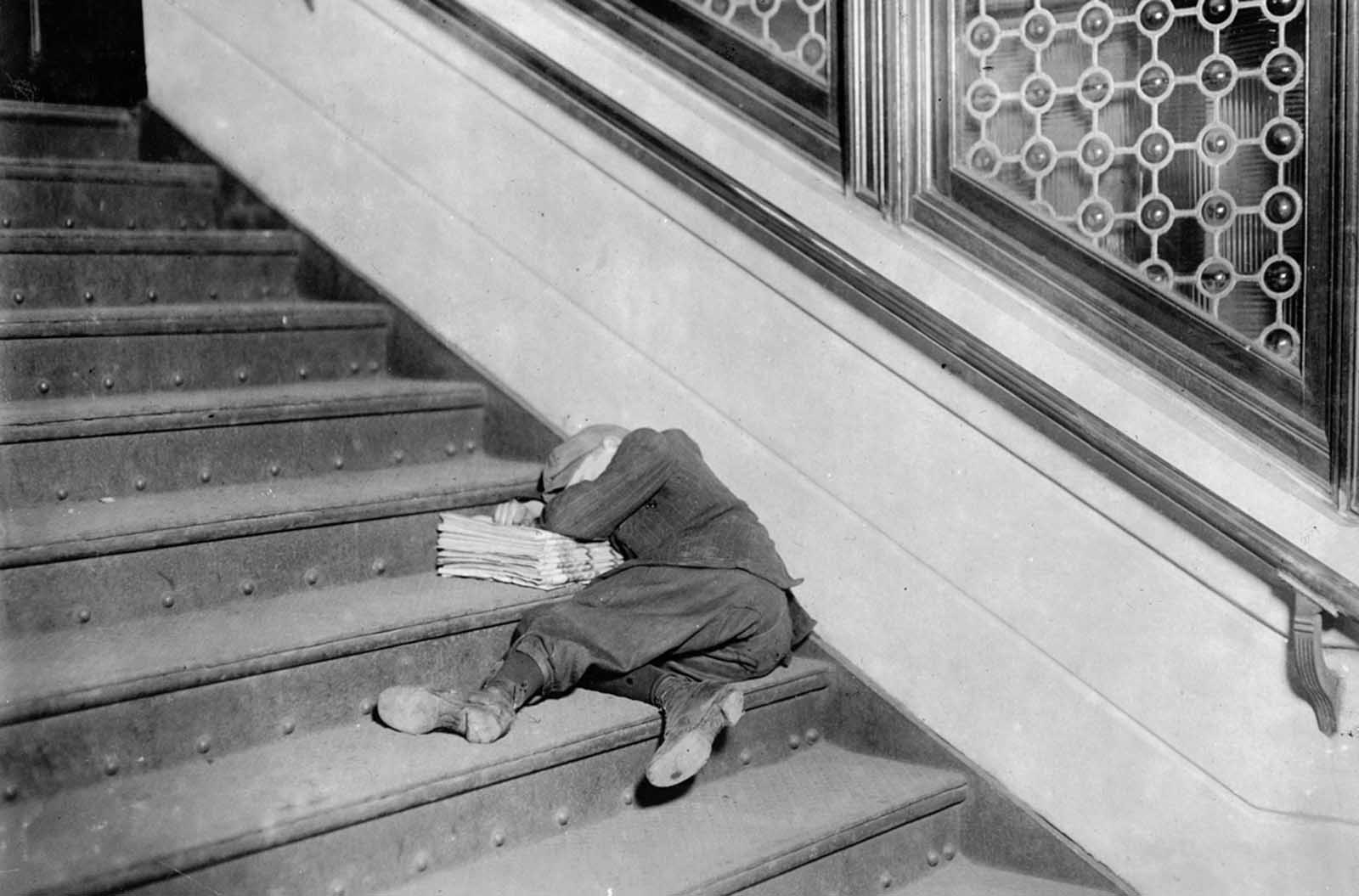 A young newsie asleep on a set of stairs with his papers, in Jersey City, New Jersey, in November of 1912.