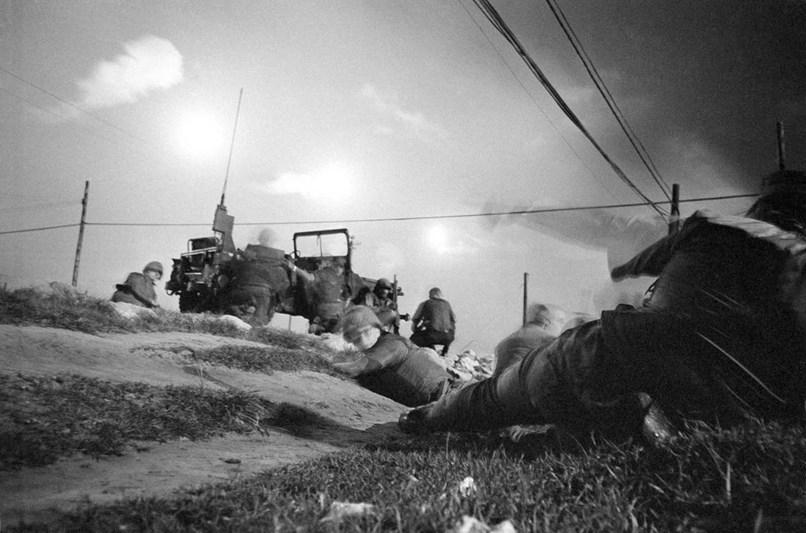U.S. air policemen take cover and leave their jeep as they come under sniper fire near Da Nang Airbase in Vietnam on January 30, 1968, after it was hit by a rocket barrage. Flares light up the Da Nang area to make it easier to spot infiltrating guerrillas.