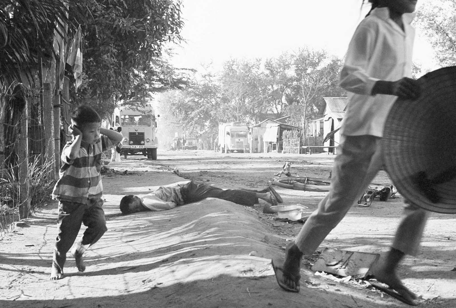 A dead civilian lies nearby as a young Vietnamese boy shields his ears from gunfire blasts and runs for cover on a Da Nang street on January 31, 1968.
