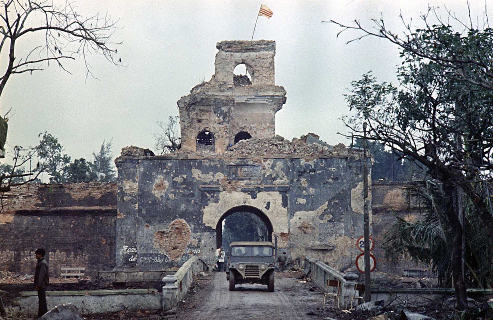 The flag of the Republic of Vietnam flies atop a tower of the main fortified structure in the old citadel as a jeep crosses a bridge over a moat in Hue during the Tet Offensive, February 1968.