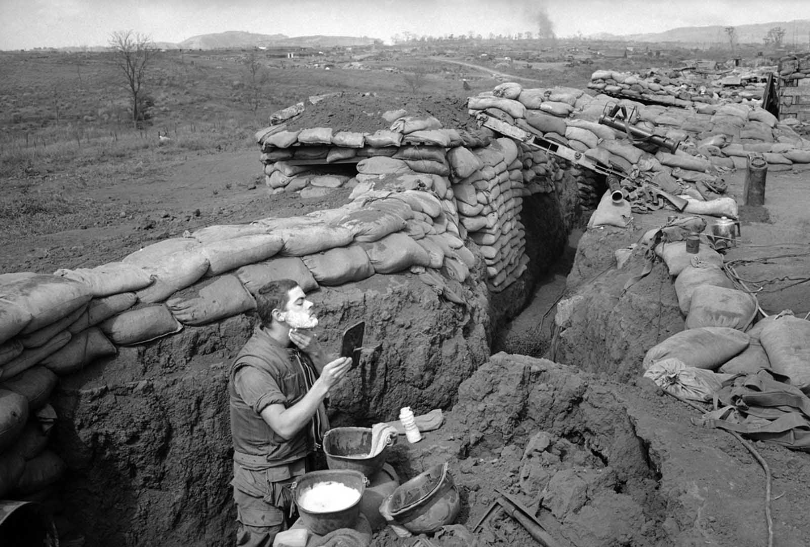 Marine Lance Corporal Roland Ball of Tacoma, Washington, wearing his flak vest, starts the day off with a shave in a trench at the Khe Sanh Base in Vietnam on March 5, 1968, which was surrounded by North Vietnamese regulars. Ball uses a helmet as a sink and a rear-view mirror taken from a military vehicle.