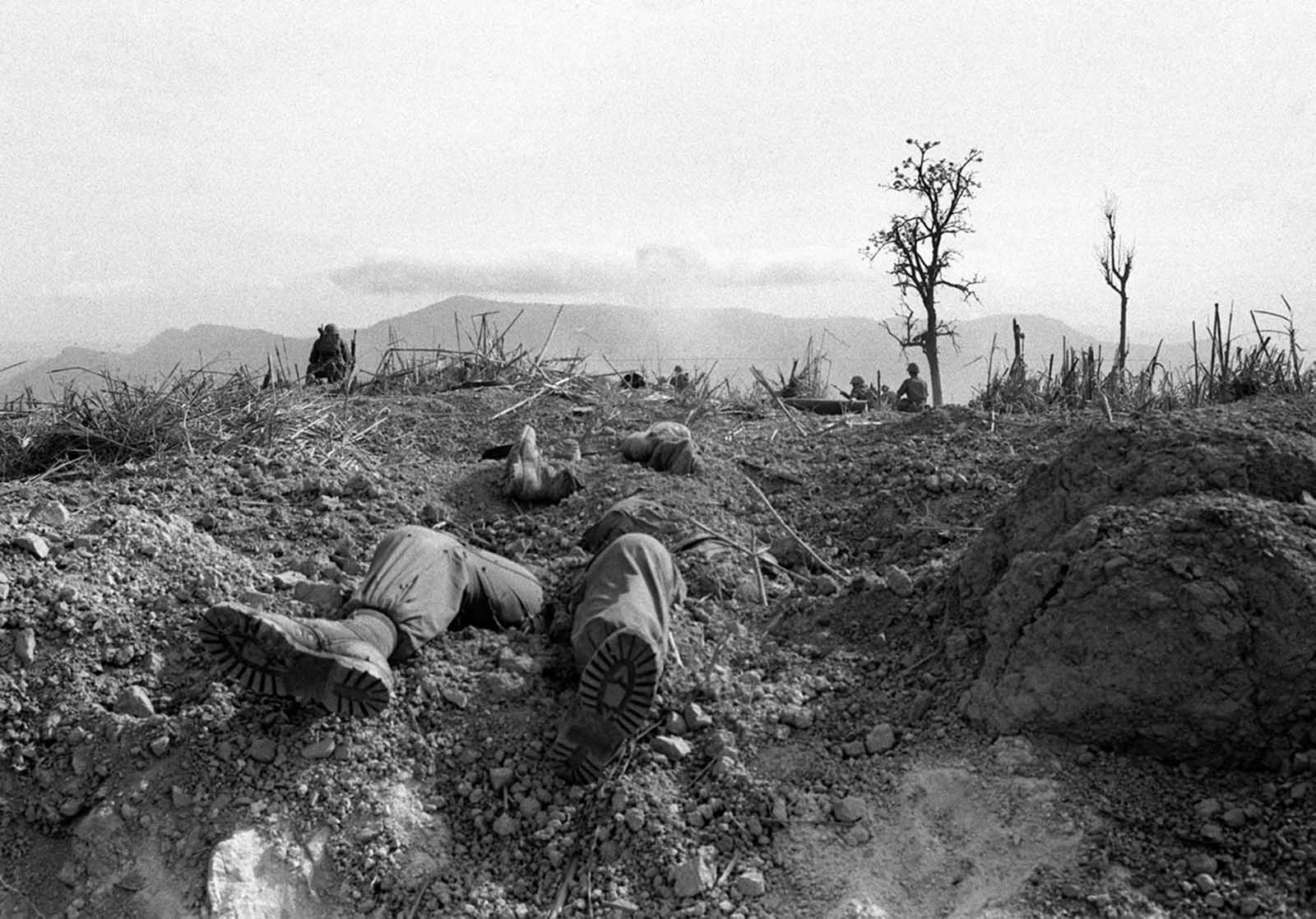 The bodies of U.S. Marines lie half buried on Hill 689, about two-and-a-half miles west of Khe Sanh, in April of 1968. Fellow Marines stand guard in the background after battling entrenched North Vietnamese troops for the hill.