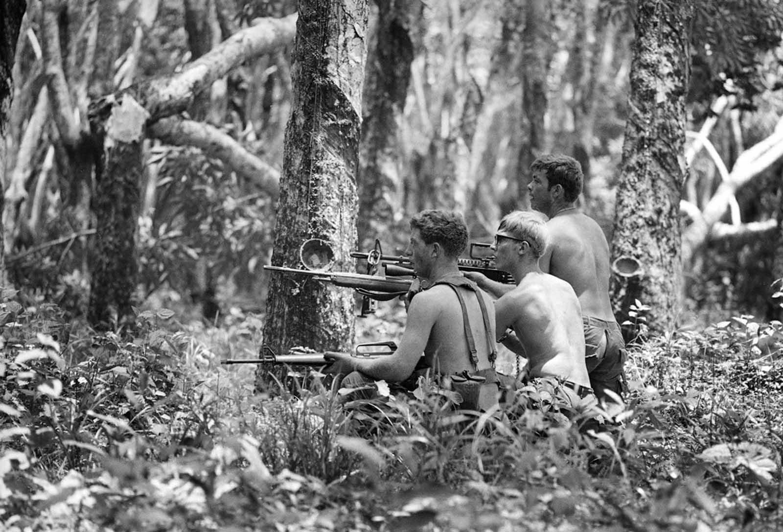 Three shirtless U.S. soldiers advance through the Mimot rubber plantation in the Fishhook region of Cambodia, on May 4, 1970, taking aim at a fleeing suspect. The rubber plantation, one of the largest in Indochina, had been in operation until just a few days earlier.