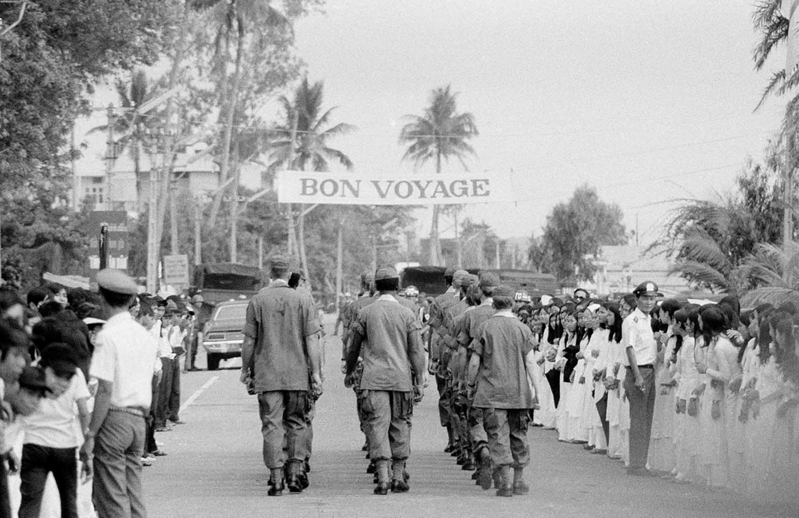 A bon voyage banner stretches overhead in Da Nang, South Vietnam, as soldiers march down a street following a farewell ceremony for some of the last U.S. troops in the country's northern military region, on March 26, 1973.
