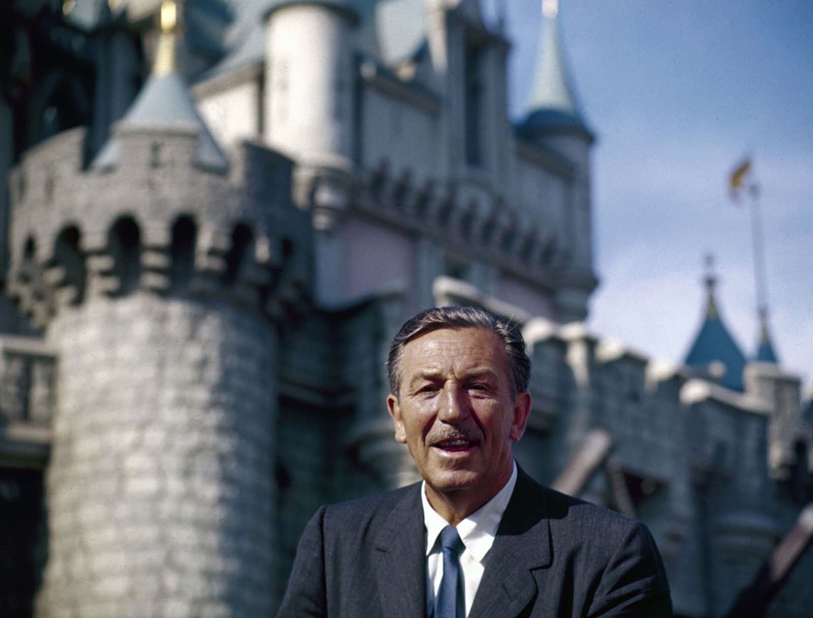 The movie producer and animator Walt Disney smiles as he stands in front of Sleeping Beauty's Castle at the grand opening of Disneyland in 1955.