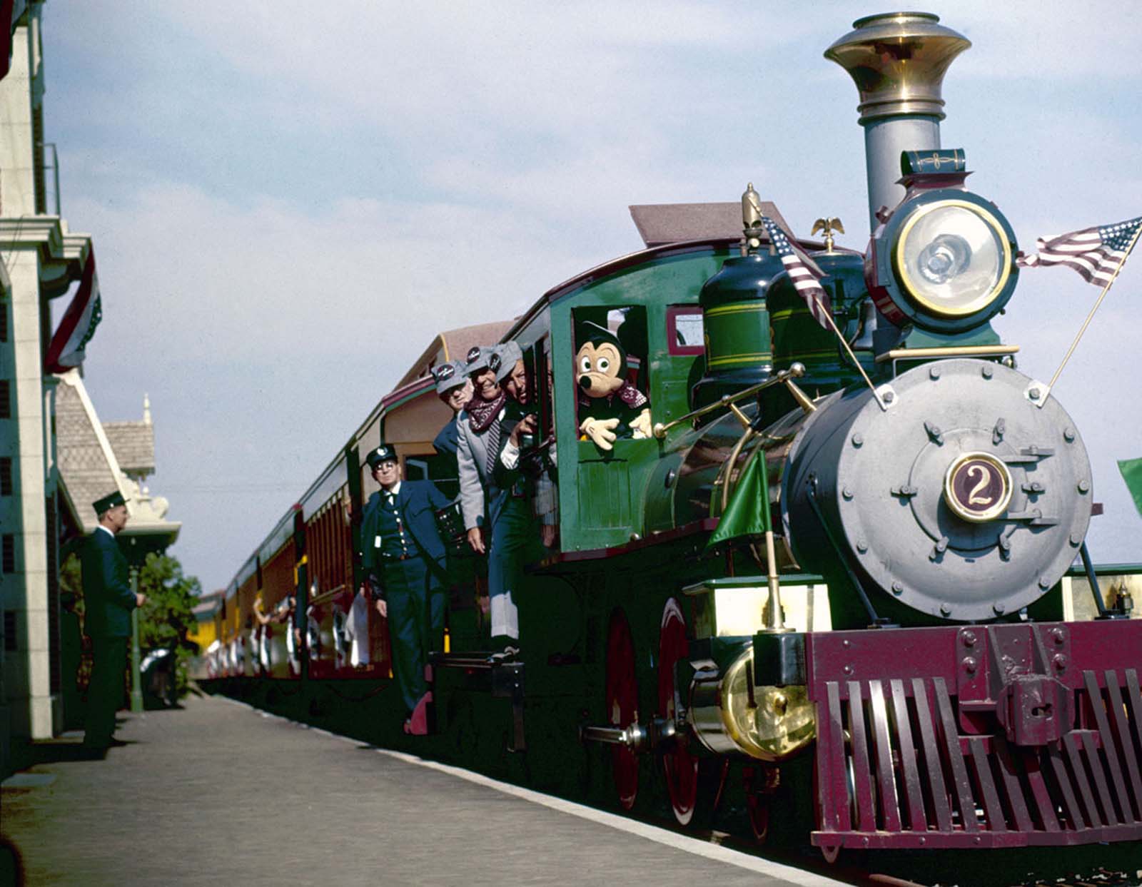 Mickey Mouse rides in the locomotive cab of a train (with Walt Disney just to his left) as it arrives at a station in Disneyland on July 18, 1955.