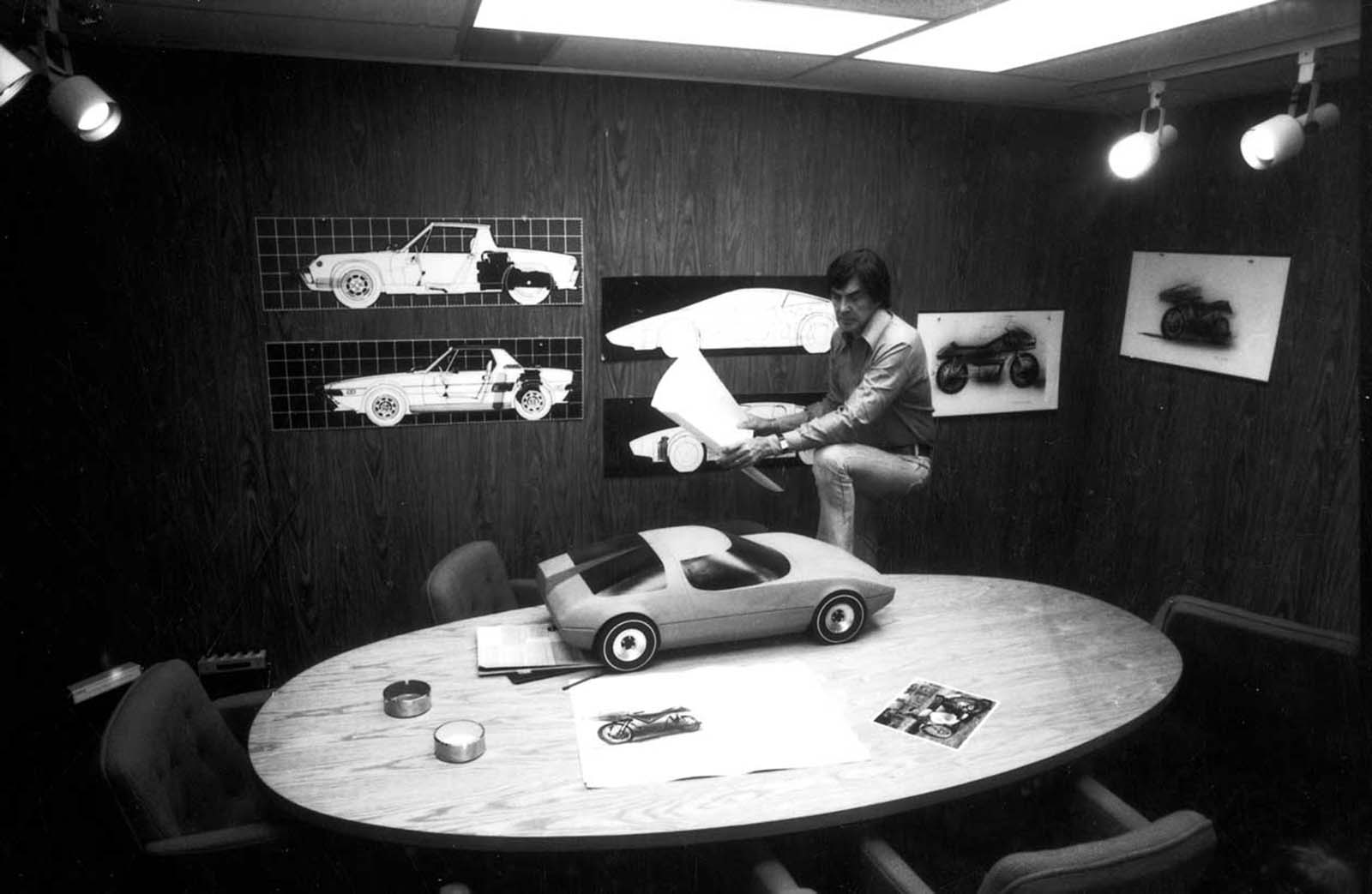 John DeLorean with various car sketches and models in a conference room in his office. 1974.