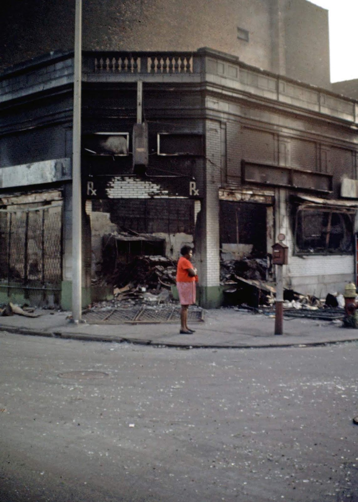 African-American woman standing on a corner of abandoned and burned buildings.