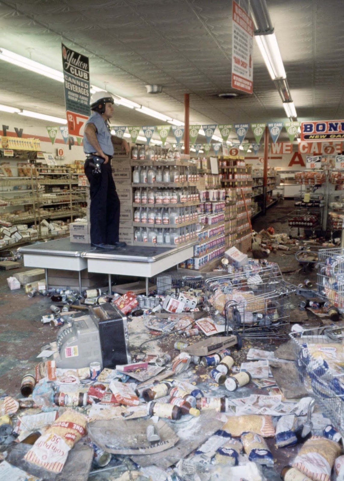 Detroit police officer standing guard over a grocery store, which was looted and damaged during the riot.