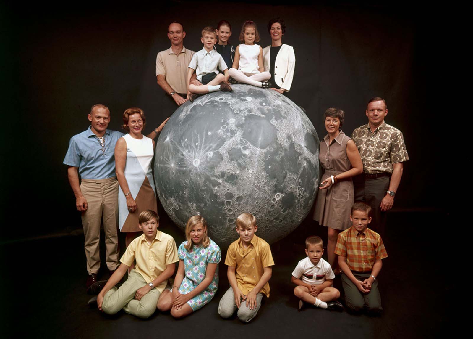 A group portrait of NASA's Apollo 11 astronauts posing with their families around a model of the moon in March 1969. Pictured are: (at top, from left) the astronaut Michael Collins; his children, Mike, Kate, and Ann; and his wife, Pat; (at left) the astronaut Buzz Aldrin; his wife, Joan; and his children, Mike, Jan, and Andy; and (at right) the astronaut Neil Armstrong; his wife, Jan; and his sons, Ricky and Mark.