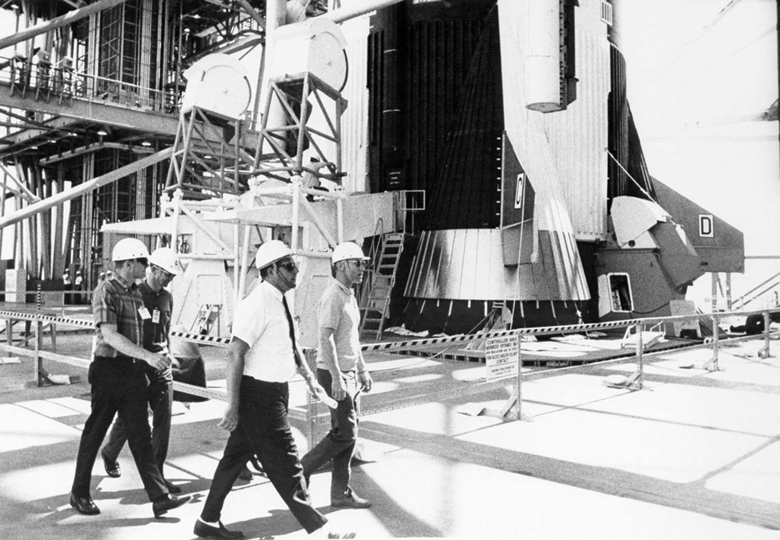 The Apollo 11 crew walks past the base of the massive Saturn V first stage during a walk-through emergency-egress test.