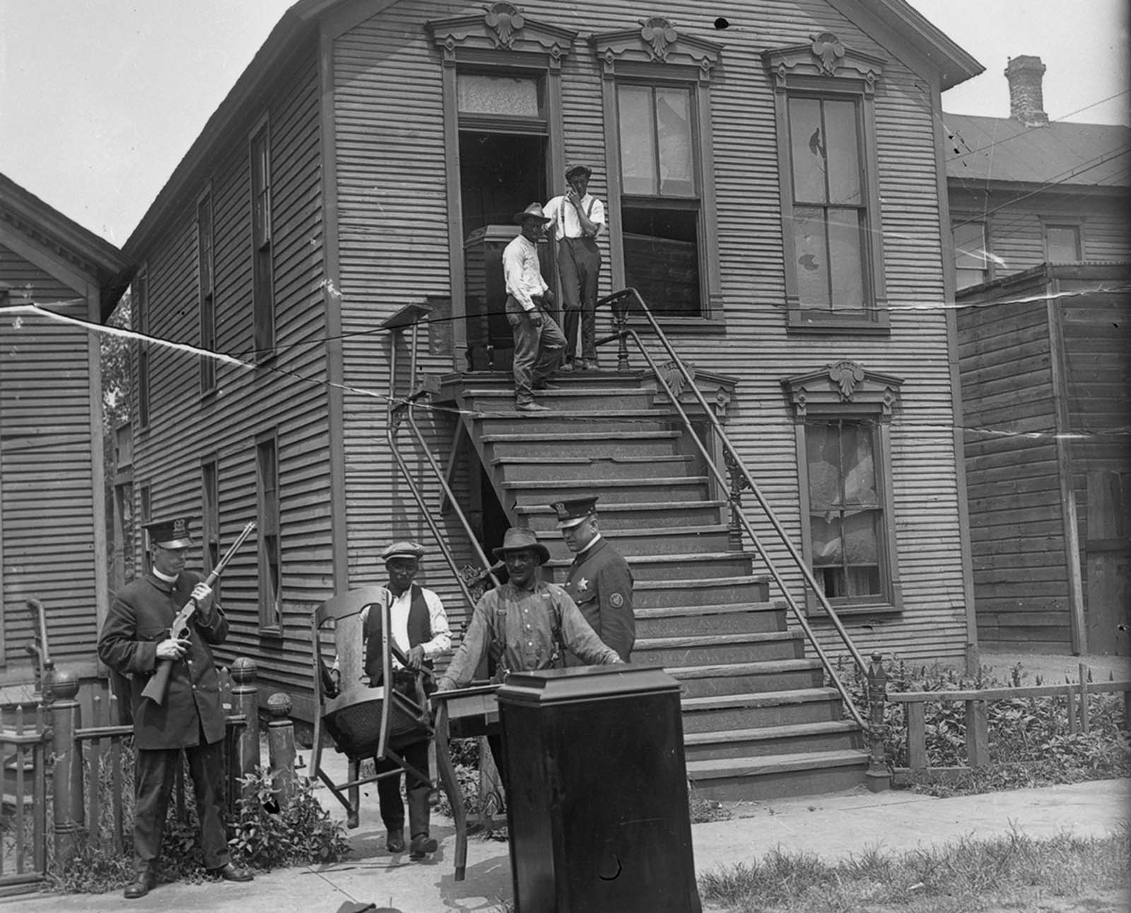 People moving out from their house, accompanied by policemen.