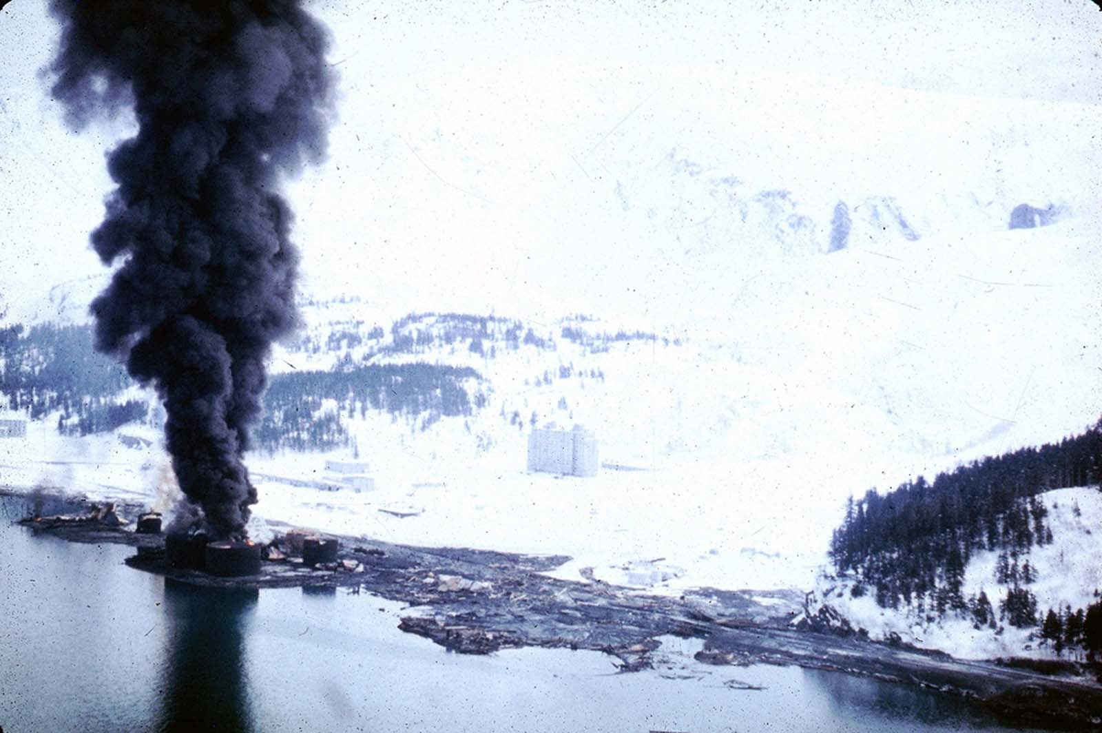 The dock area, a tank farm, and railroad facilities in Whittier, Alaska were severely damaged by surge-waves developed by underwater landslides in Passage Canal, on March 27, 1964. The waves inundated the area of darkened ground, where the snow was soiled or removed by the waves.