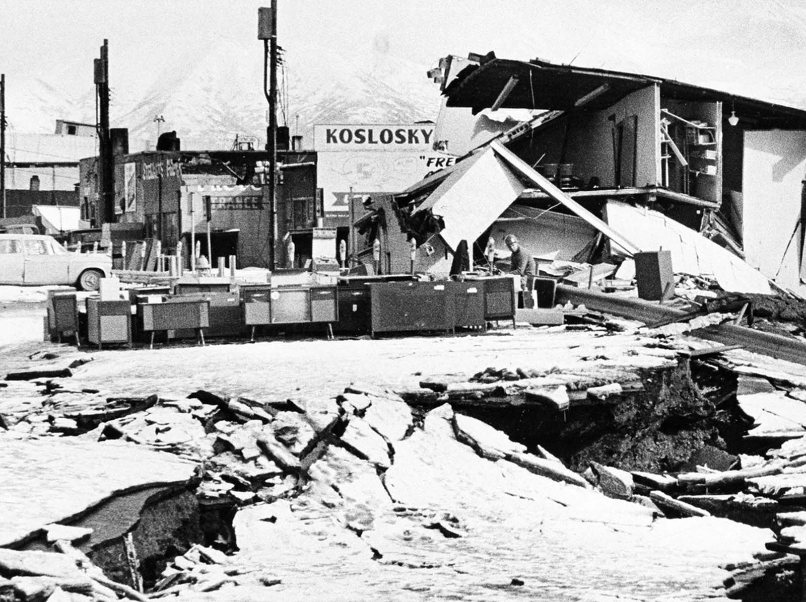 An unidentified man sits at a desk beside hi-fi sets moved to the middle of Fourth Avenue in Anchorage on March 31, 1964. The items were moved from a store that was demolished in the earthquake.
