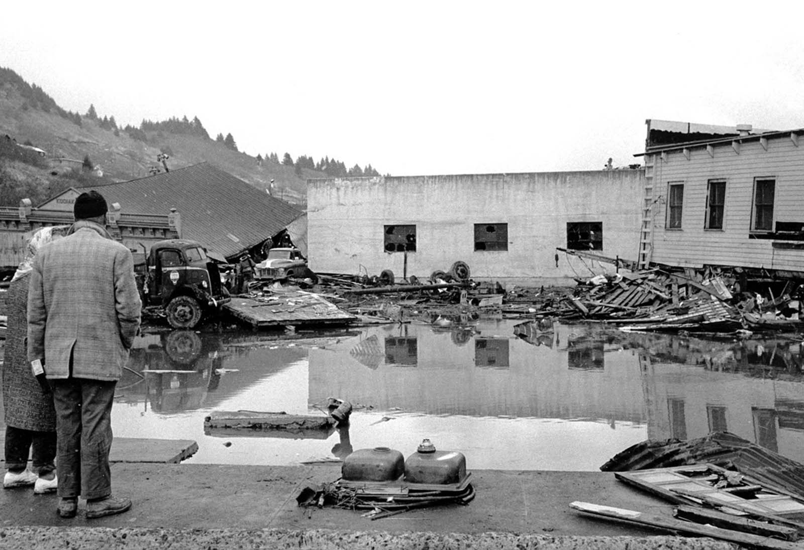 A forlorn couple stands on a concrete dock viewing the remains of the Kodiak waterfront on March 29, 1964.