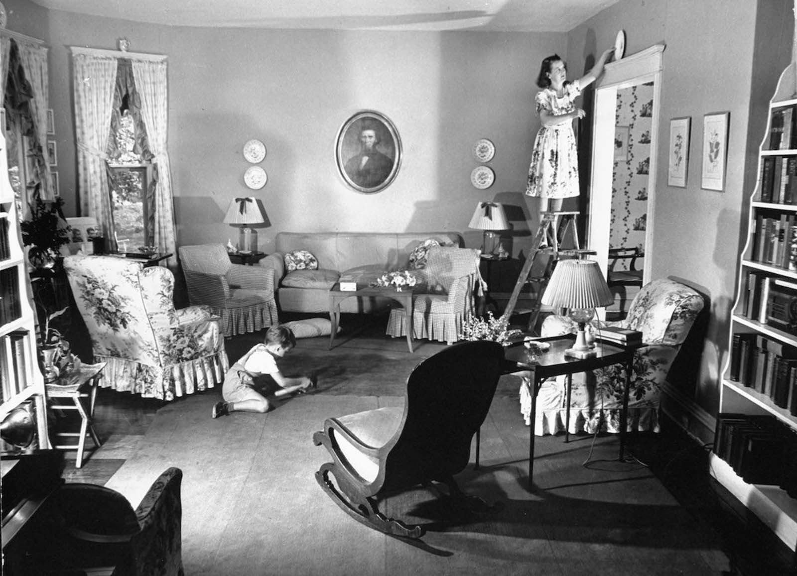 Jane standing on ladder to place special china plate as decoration above the doorway in the living room, which she decorated herself, as her son Tony plays on the floor.
