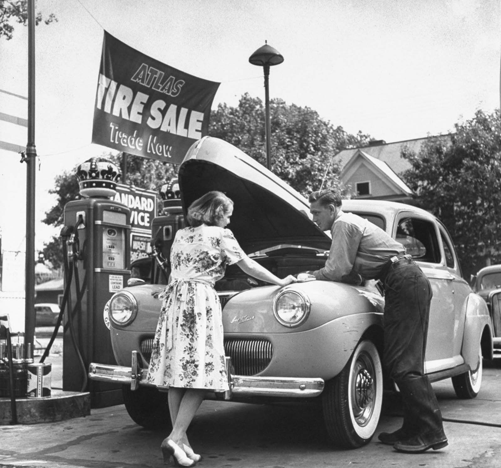 Jane conferring with a mechanic at gas station about the car she uses to chauffeur her husband to and from his office, plus get the children back and forth to school.