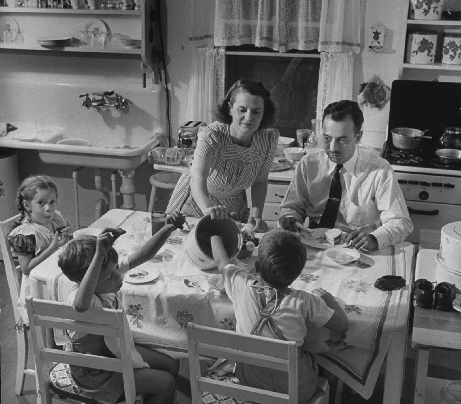 Jane serving lunch to her husband Gilbert, who has come home from the office a few minutes away, and her ever-present kids.