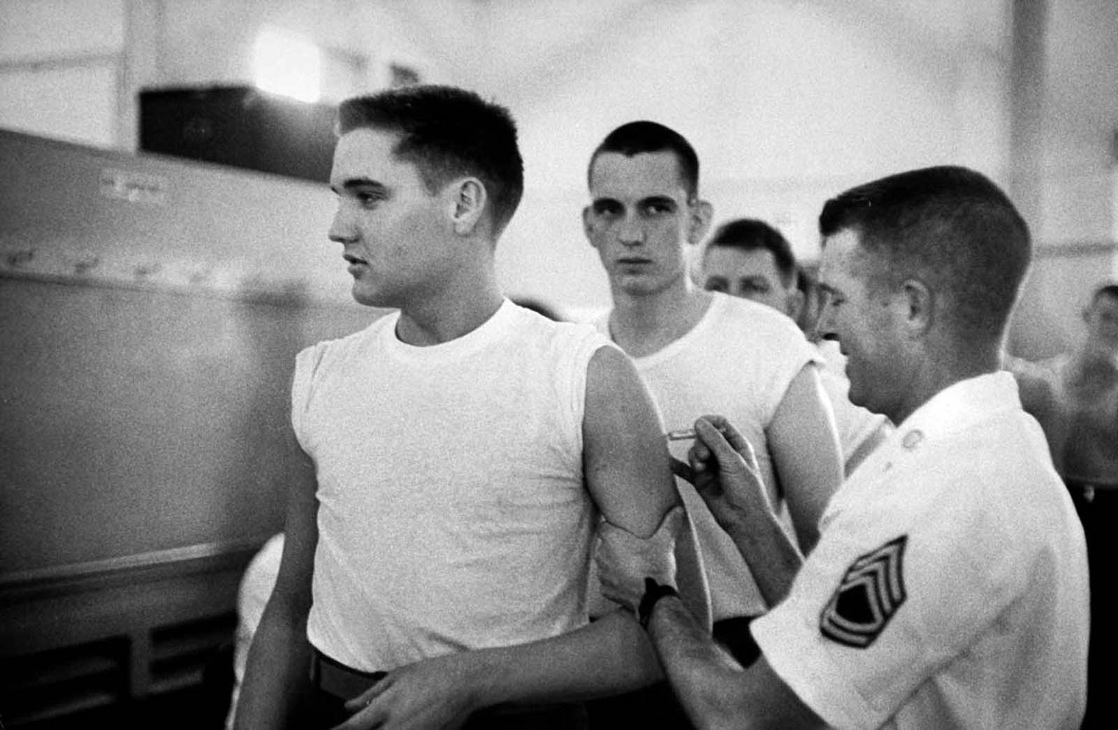 Presley in t-shirt, getting a shot from an Army doctor during his pre-induction physical at Kennedy Veterans Hospital.
