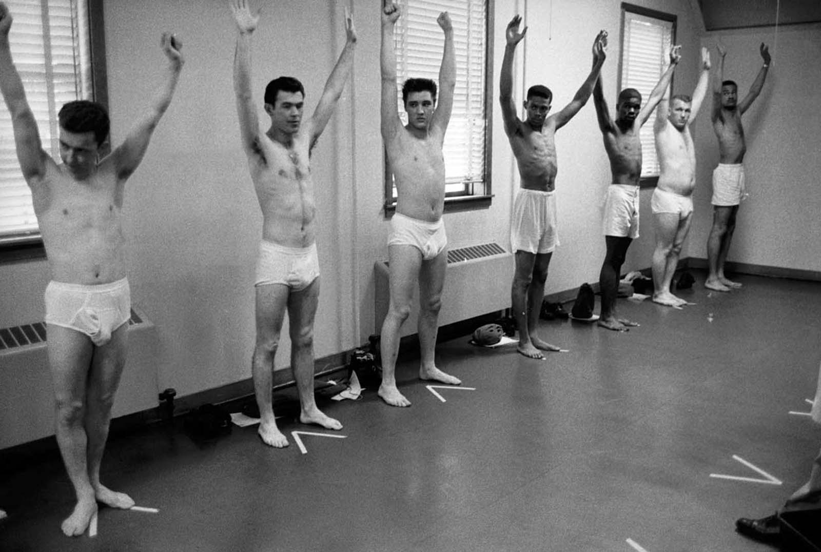 Wearing only underwear, Pvt. Elvis Presley raises his arms along with several other inductees during an inspection at Ft. Chaffee.