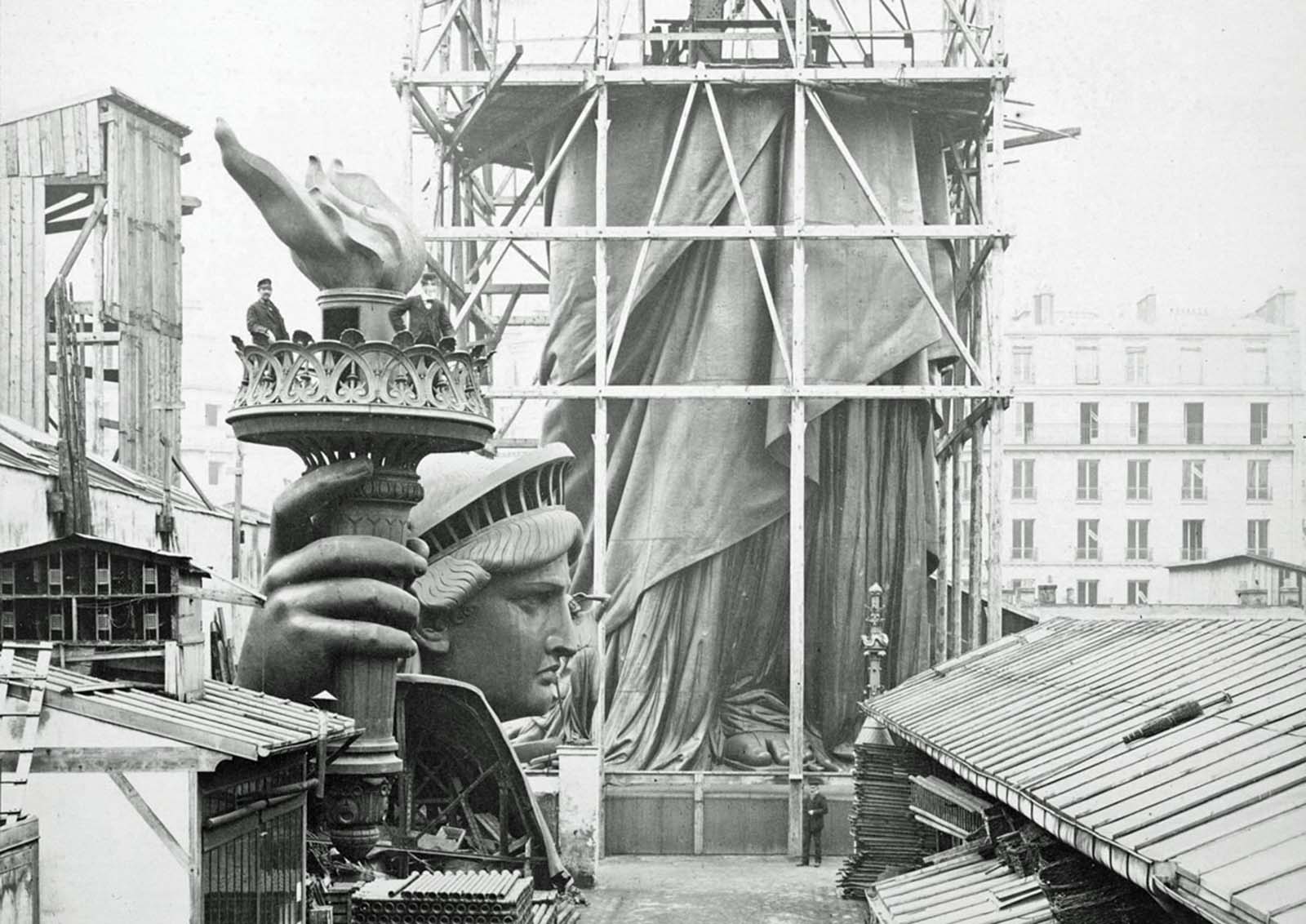 Assemblage of the Statue of Liberty in Paris, showing the bottom half of the statue under scaffolding, with the head and torch at its feet, photographed in 1883.