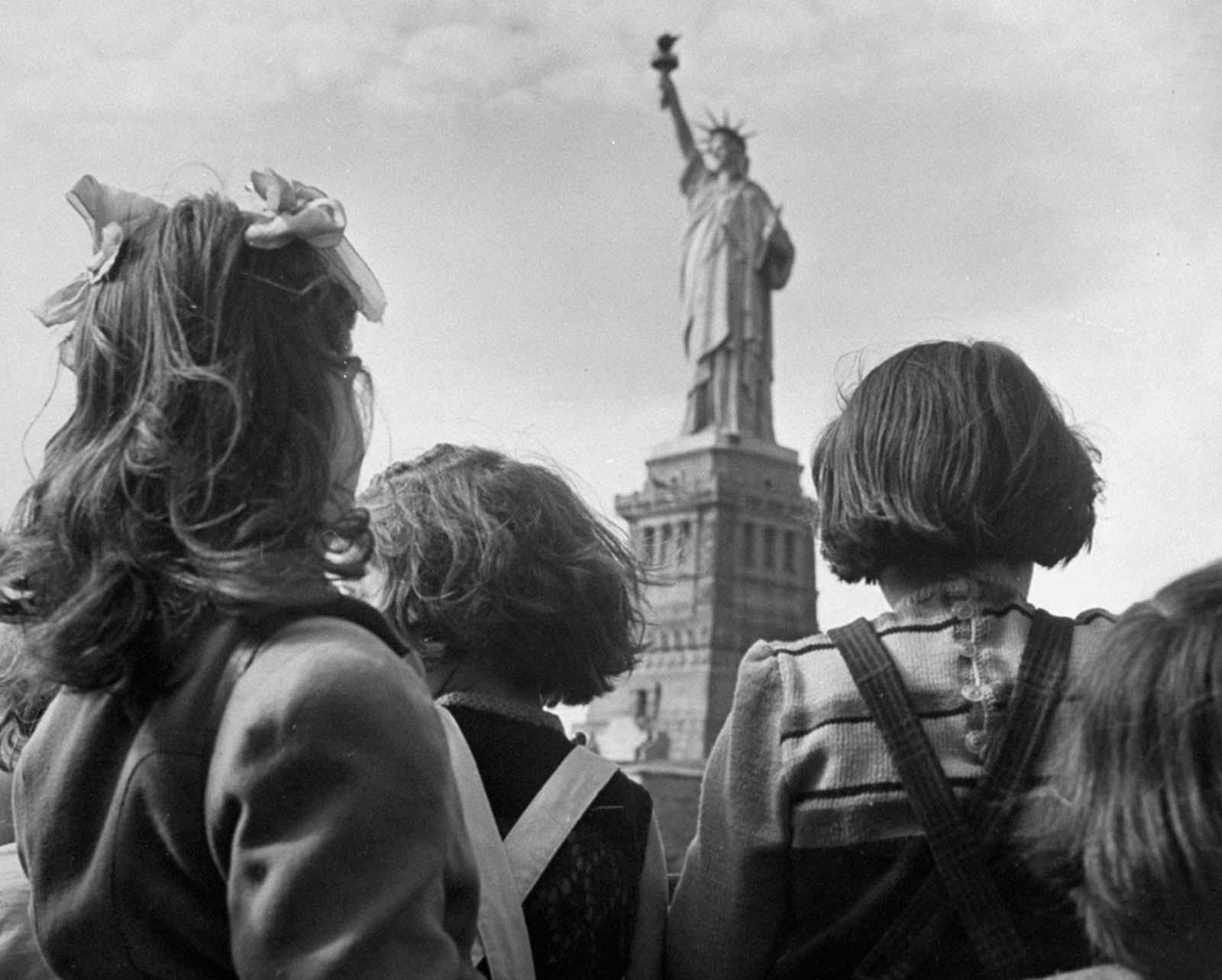 In 1946, refugee children gaze at the Statue of Liberty from the railing of a boat.